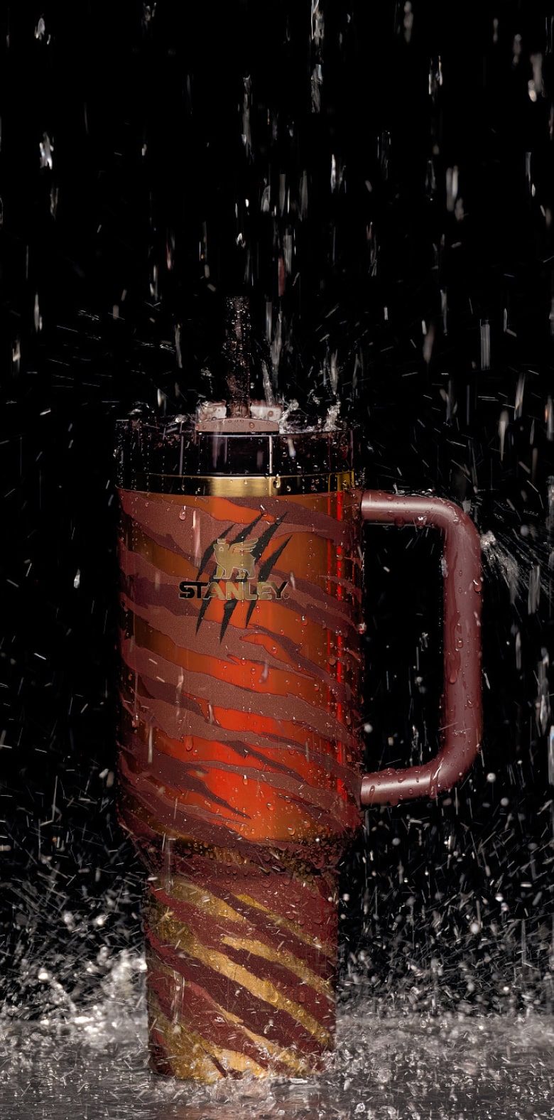 Stanley insulated travel mug with tiger stripe design and water splashing on black background