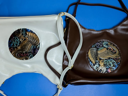 White and brown leather handbags with embossed elephant designs on a blue background