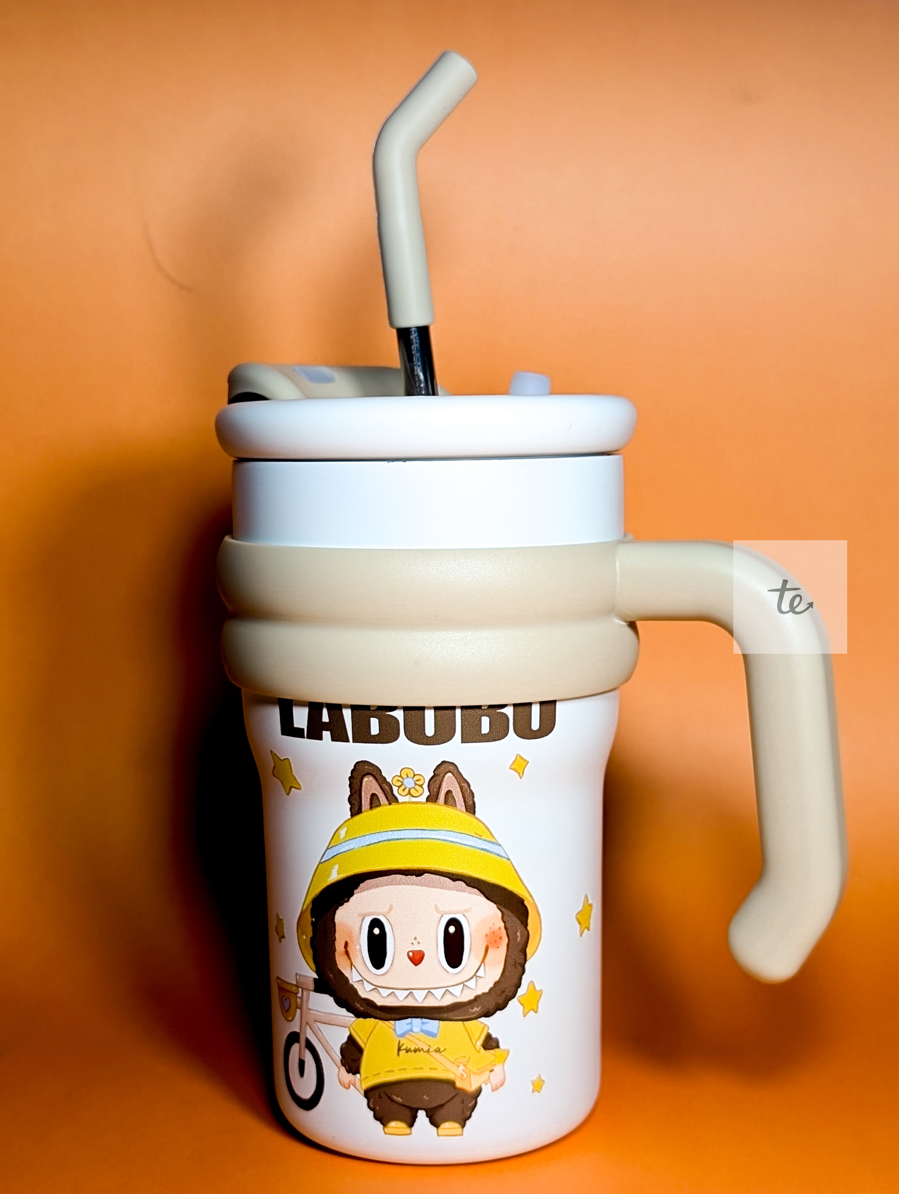White and beige sippy cup with handle featuring a cartoon character in a yellow outfit on orange background
