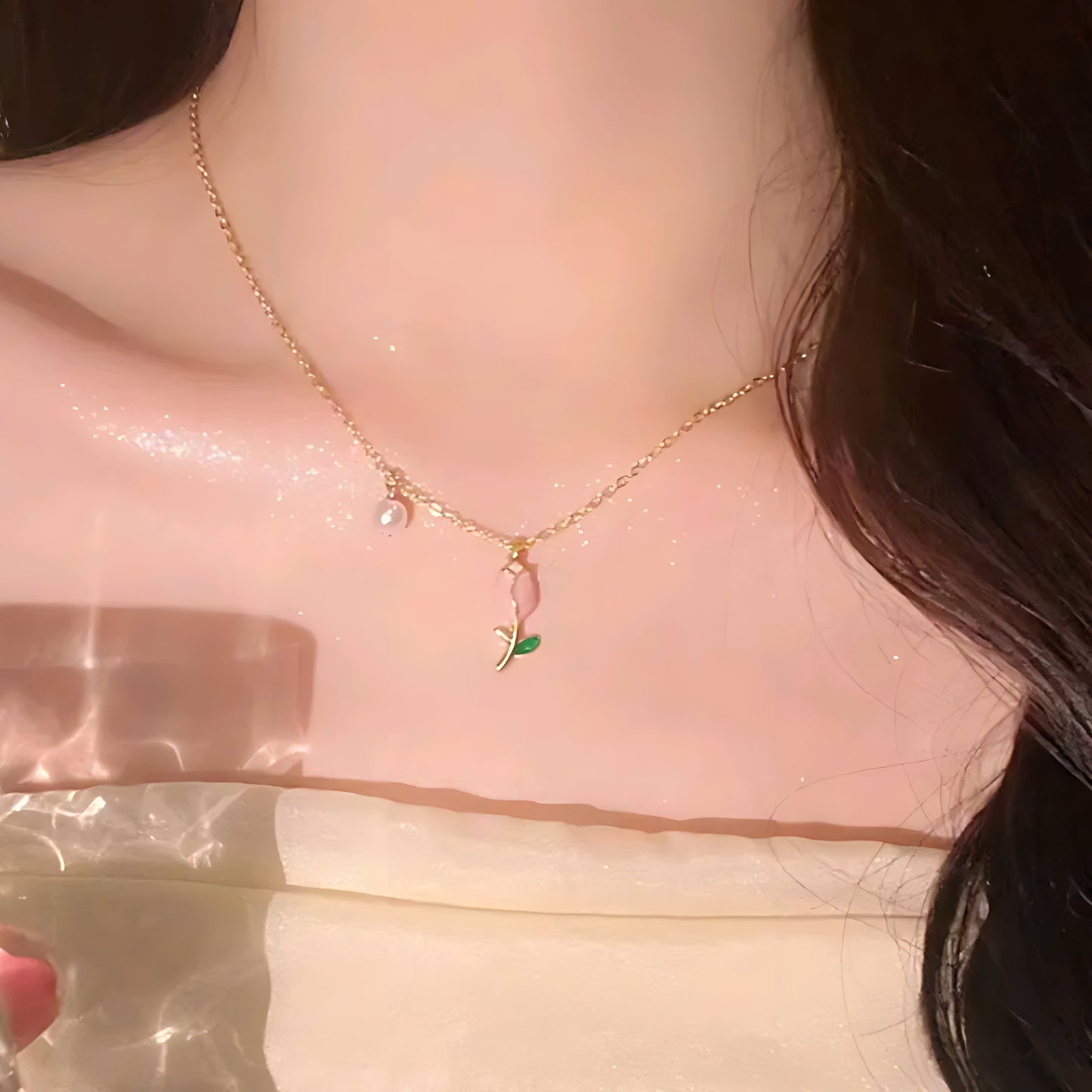 Close-up of woman wearing gold necklace with pink rose charm and small pearl pendant on bare neck