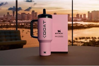 Pink Stanley GOAT tumbler with Messi branding on table, city skyline and sunset in background