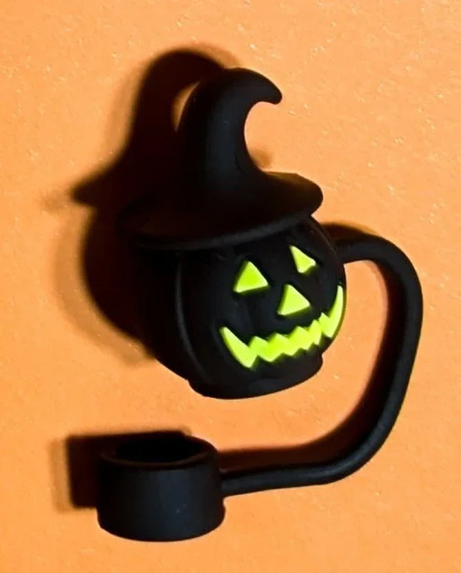 Black Halloween pumpkin with glowing yellow eyes and mouth wearing a witch hat against orange background