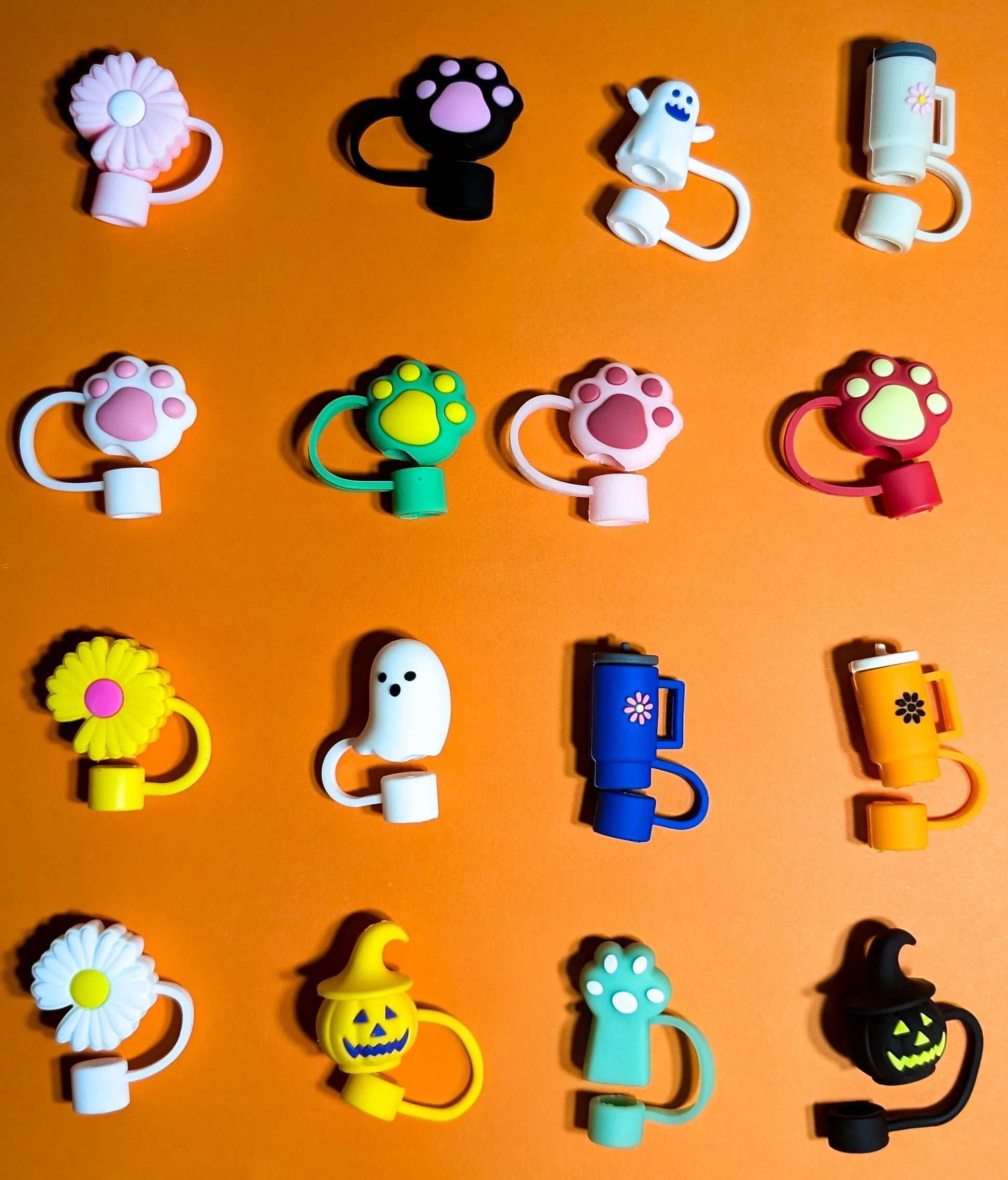 Colorful silicone finger ring caps with cute designs including flowers, paws, ghosts, mugs, and Halloween pumpkins on orange background