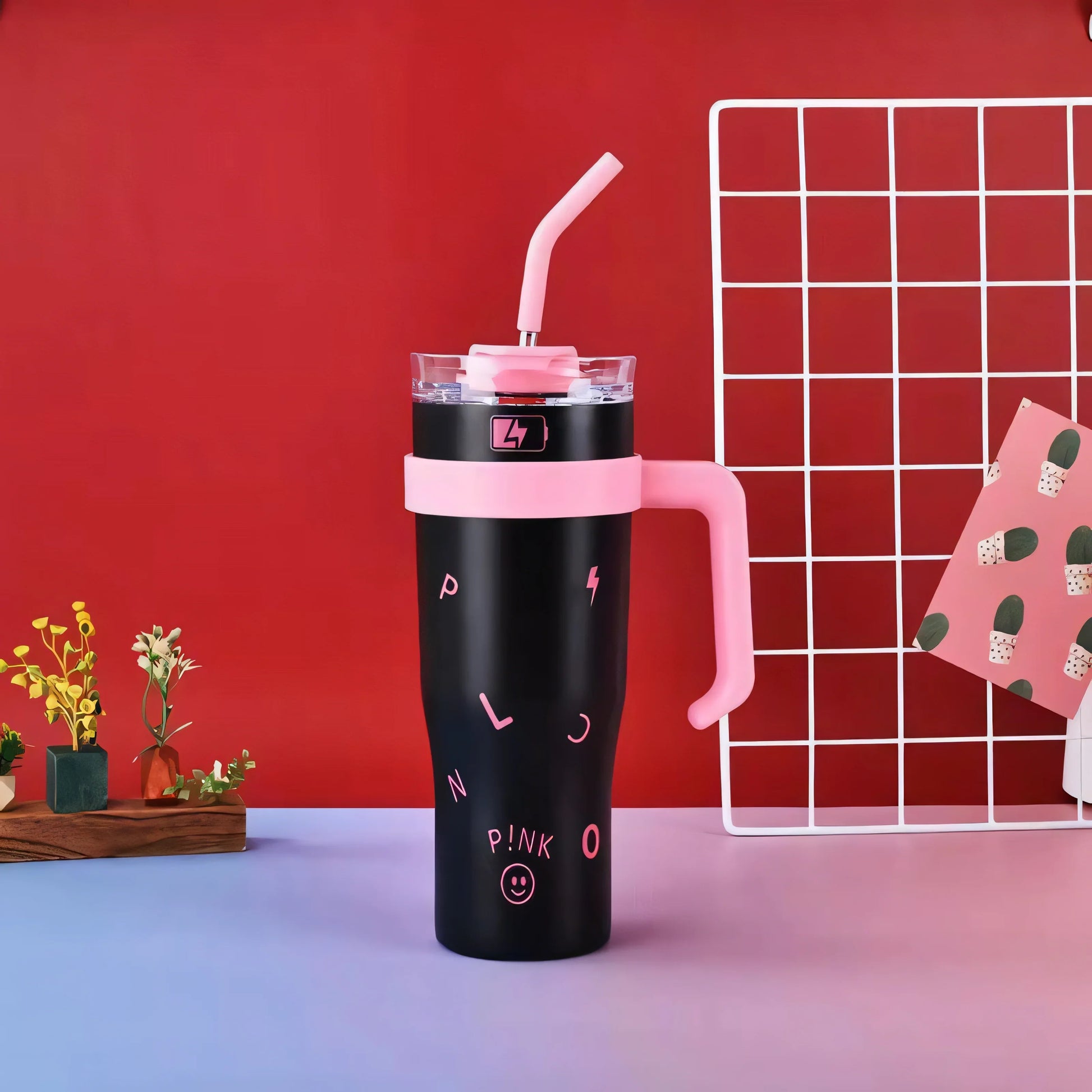 Black and pink insulated water bottle with straw and letters on a colorful table against a red wall