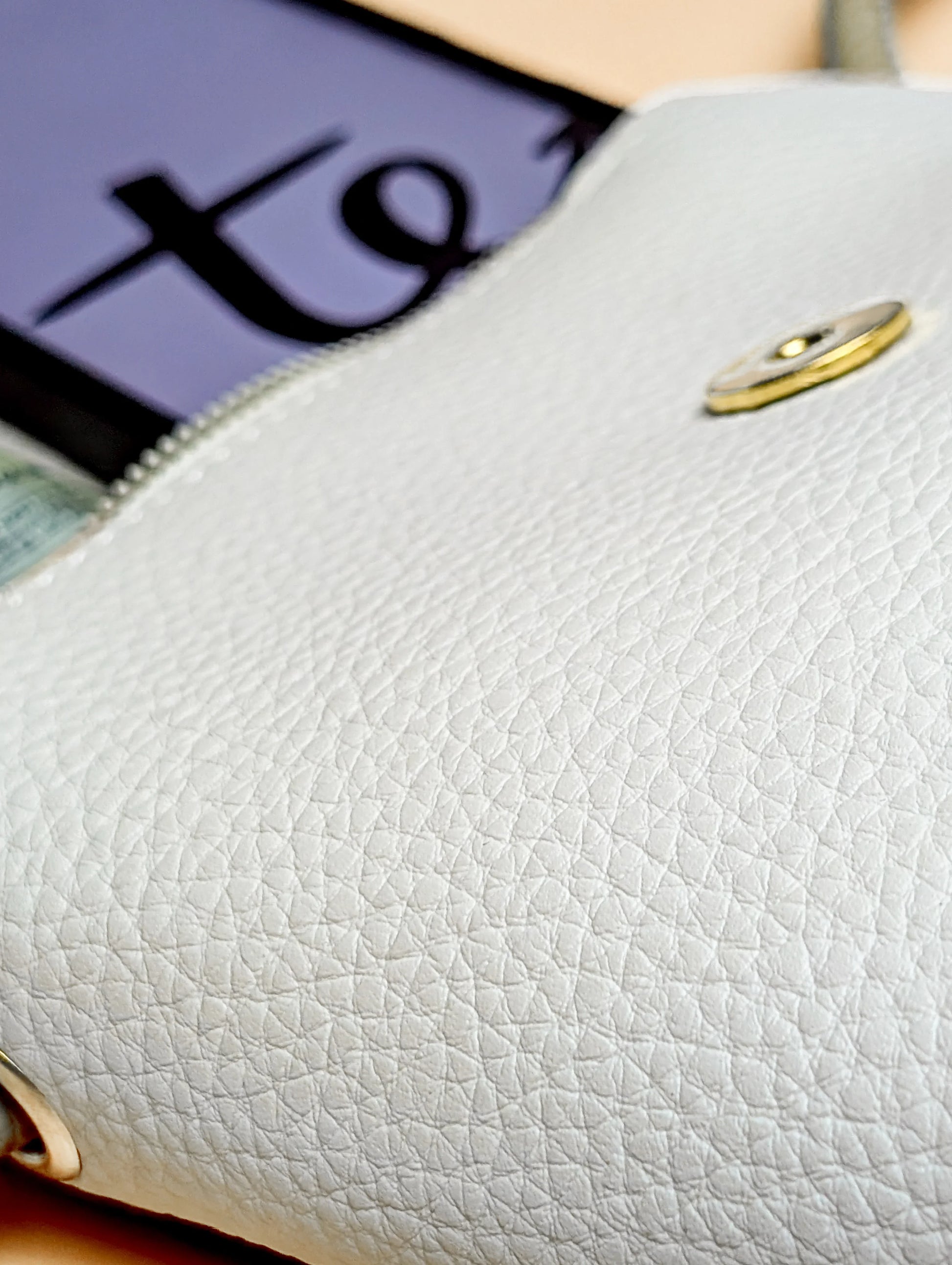 Close-up of white textured leather pouch with gold button and partially visible tablet screen