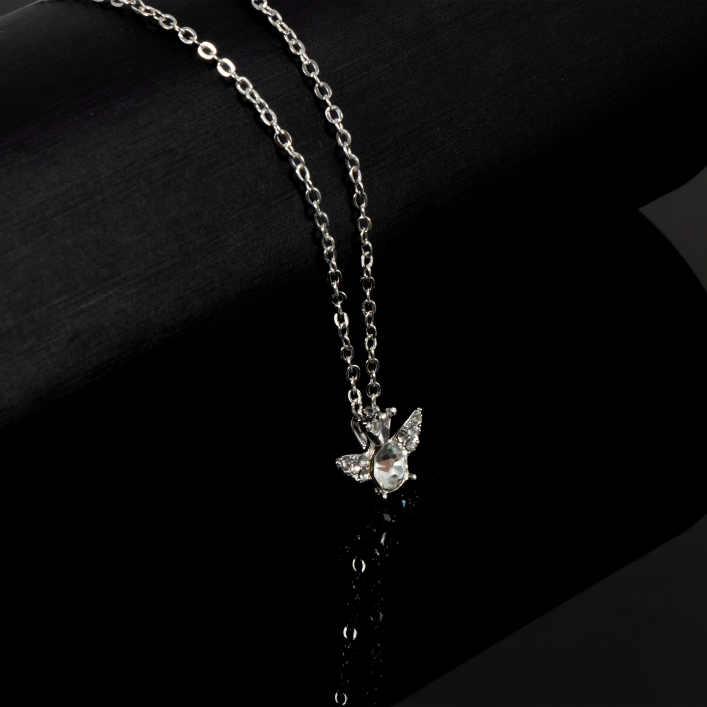 Silver necklace with angel wing pendant featuring clear crystal on black background