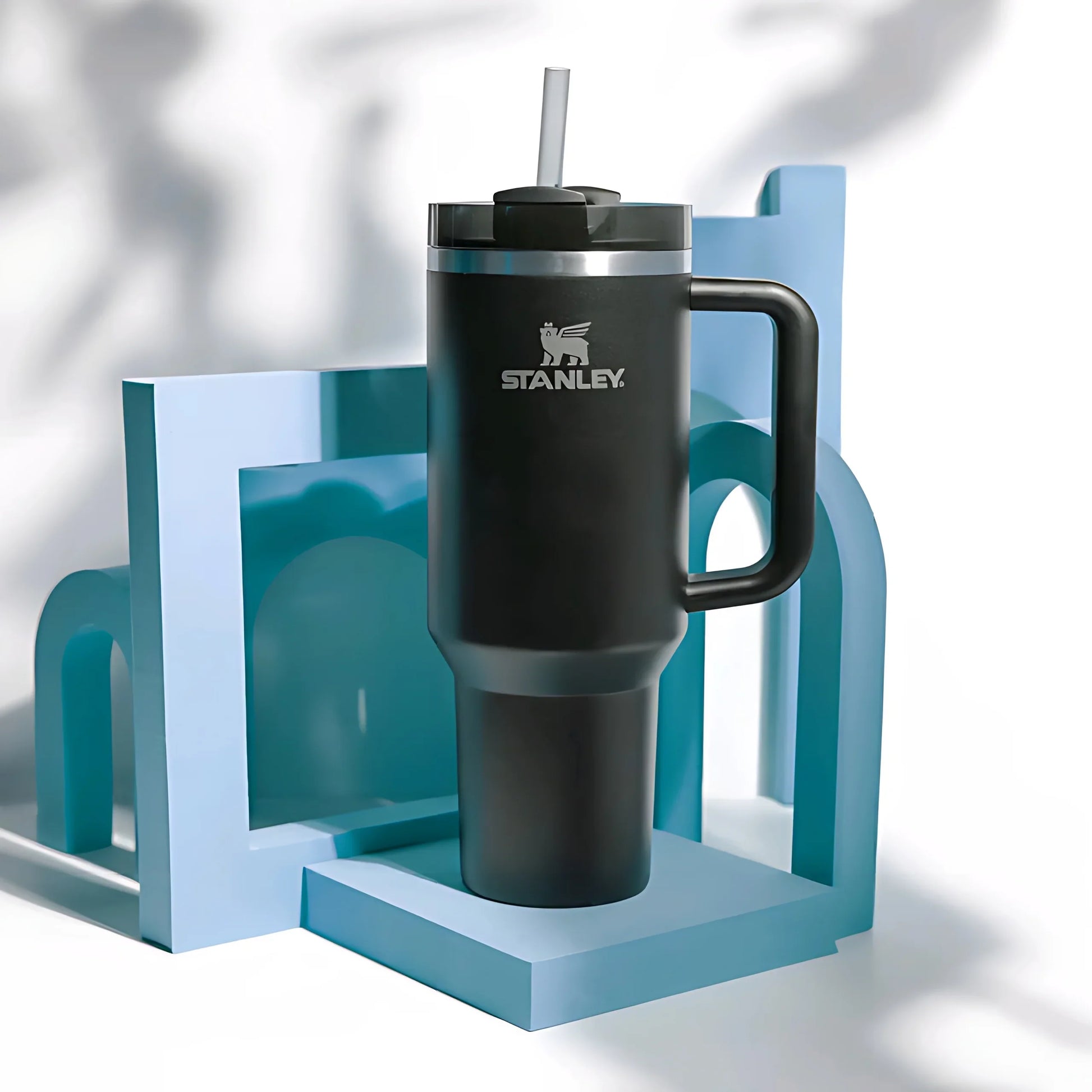 Black Stanley insulated travel mug with handle and straw on blue geometric stand