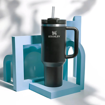 Black Stanley insulated travel mug with handle and straw on blue geometric stand
