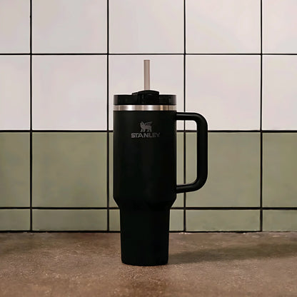 Black Stanley travel mug with handle and straw on kitchen counter with white and green tiled wall