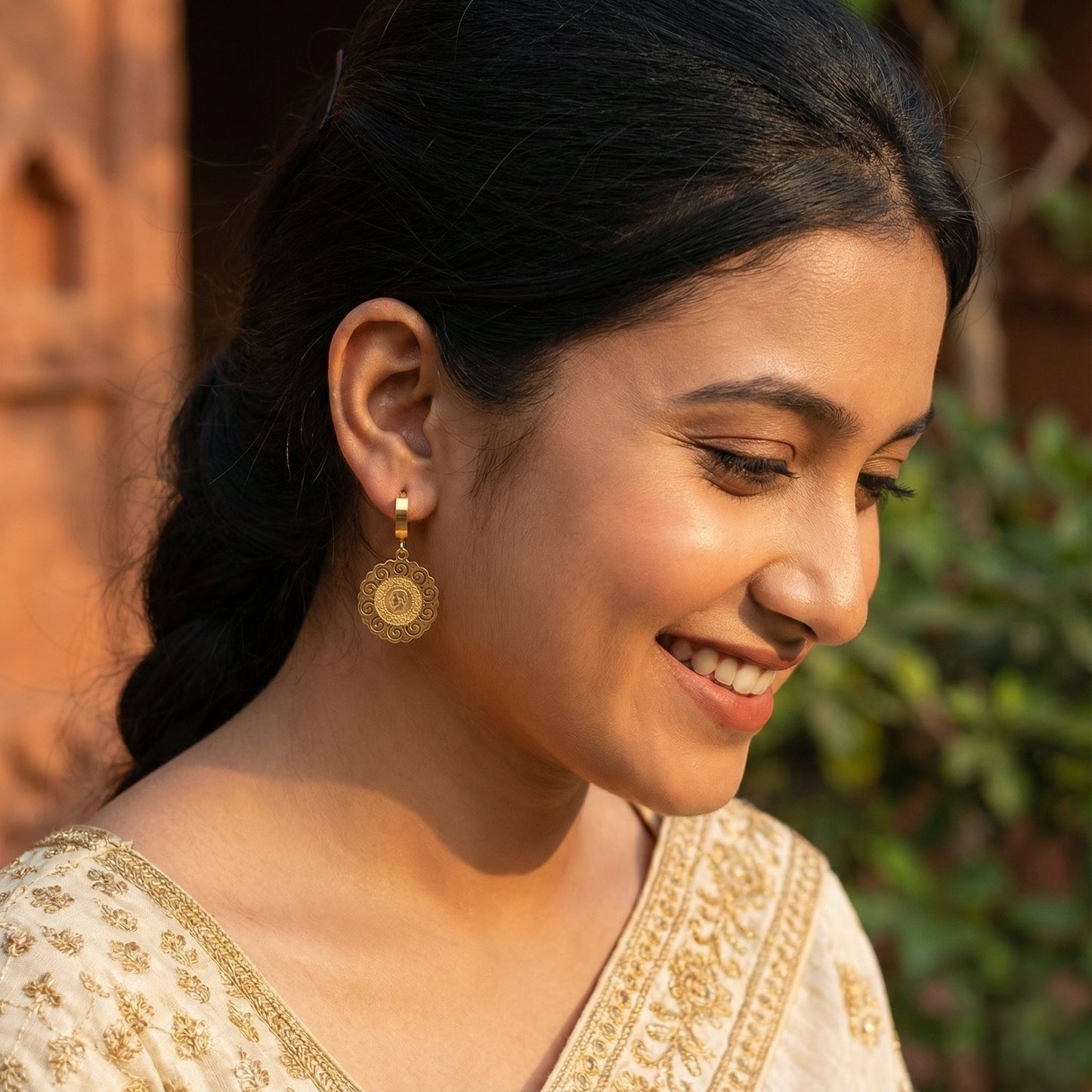 Close-up of smiling woman wearing gold traditional earrings and embroidered beige outfit outdoors