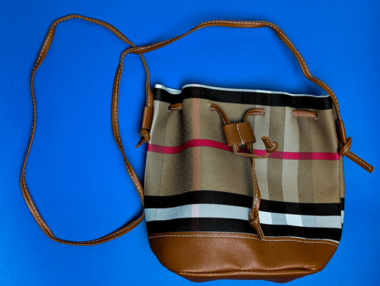 Brown leather and plaid fabric crossbody bucket bag with adjustable strap on blue background