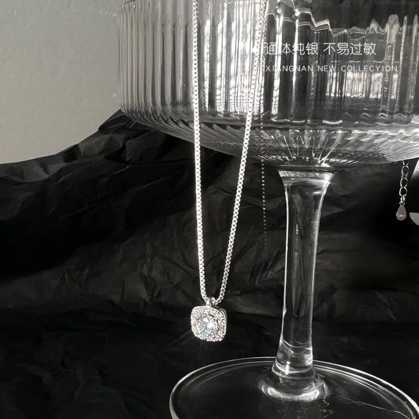 Silver pendant necklace with sparkling gem hanging on elegant glass stemware against black fabric background
