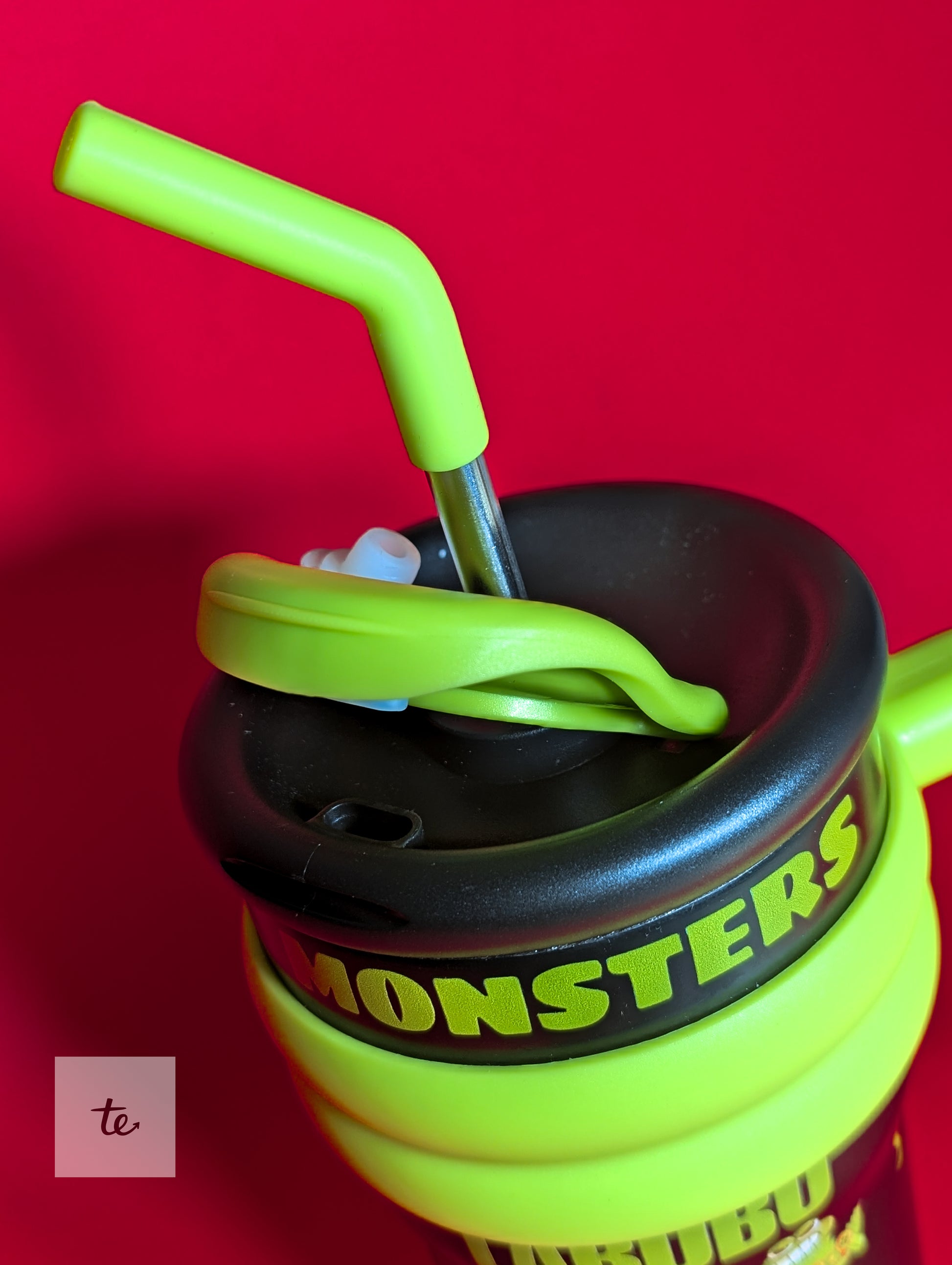 Close-up of a green and black Monsters reusable cup lid with a bent straw against red background