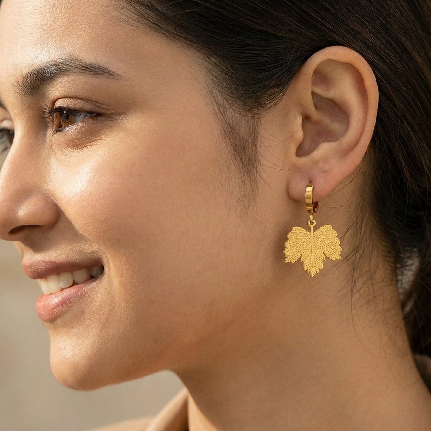 Close-up of woman's ear wearing gold leaf-shaped dangle earrings with textured detailing