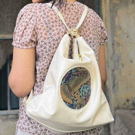 White leather backpack with embossed colorful elephant design worn by person in floral pink blouse