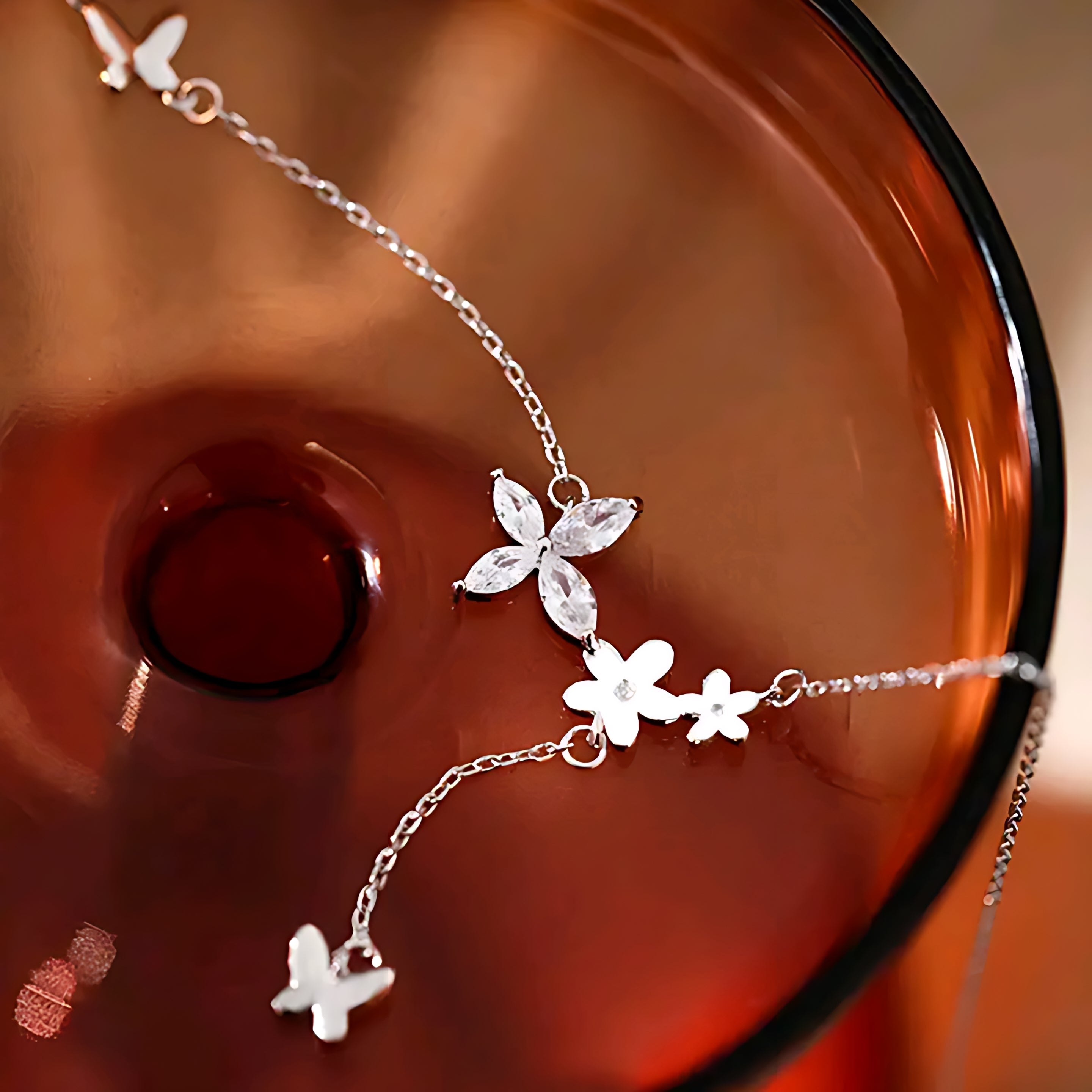 Delicate silver necklace with floral and butterfly charms displayed on a smooth amber glass surface