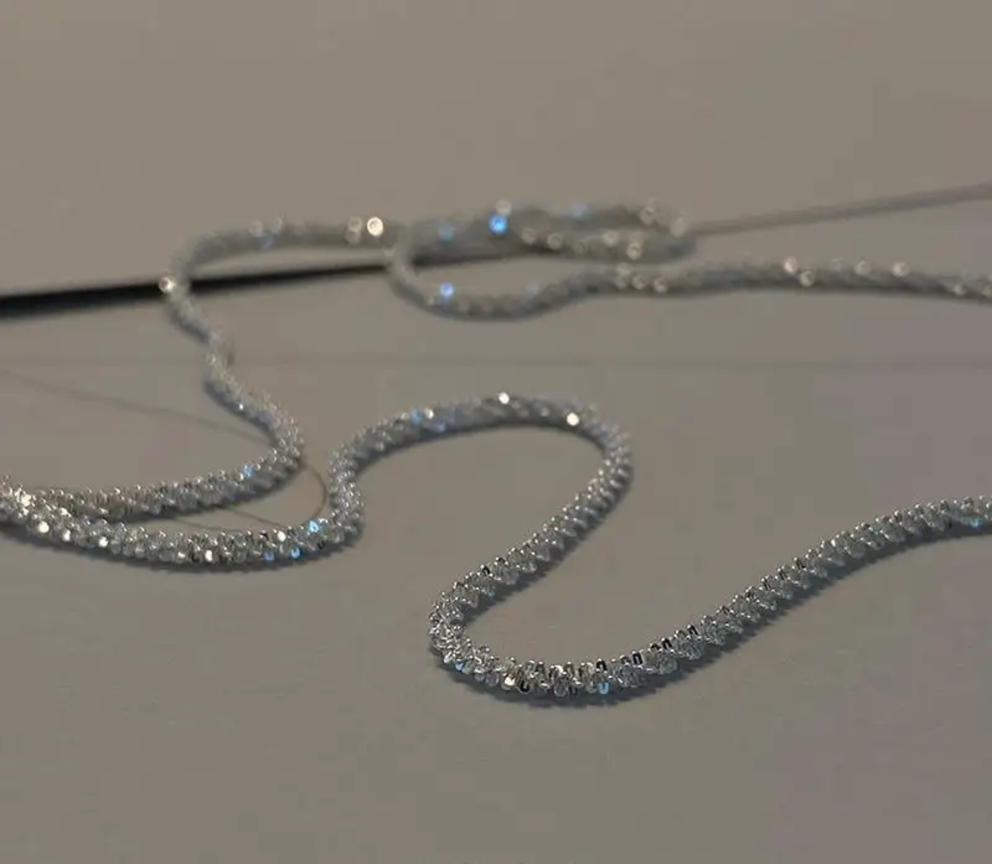 Close-up of a sparkling silver rhinestone chain necklace on a gray surface