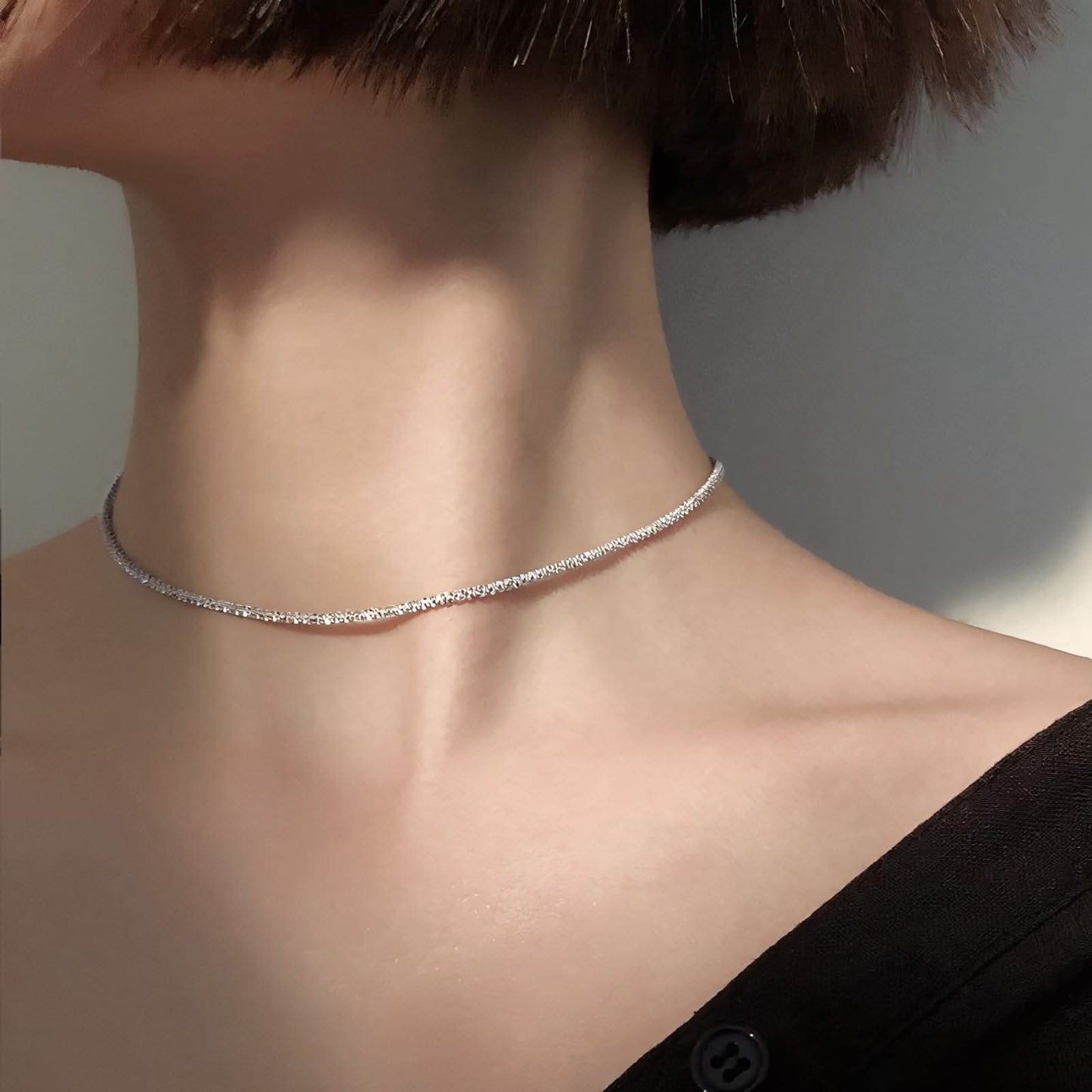 Close-up of a woman's neck wearing a thin silver choker necklace with short brown hair and black top