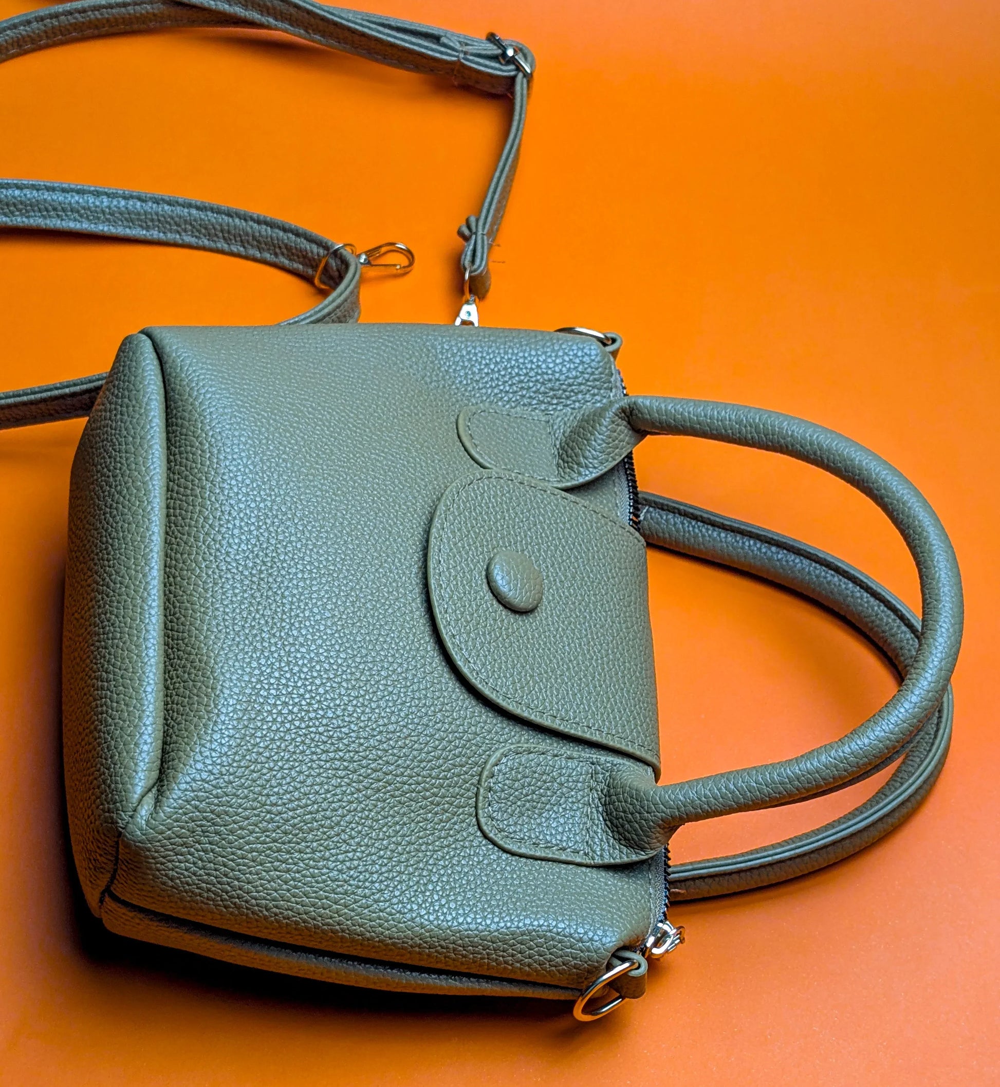 Green textured leather handbag with handles and detachable strap on orange background