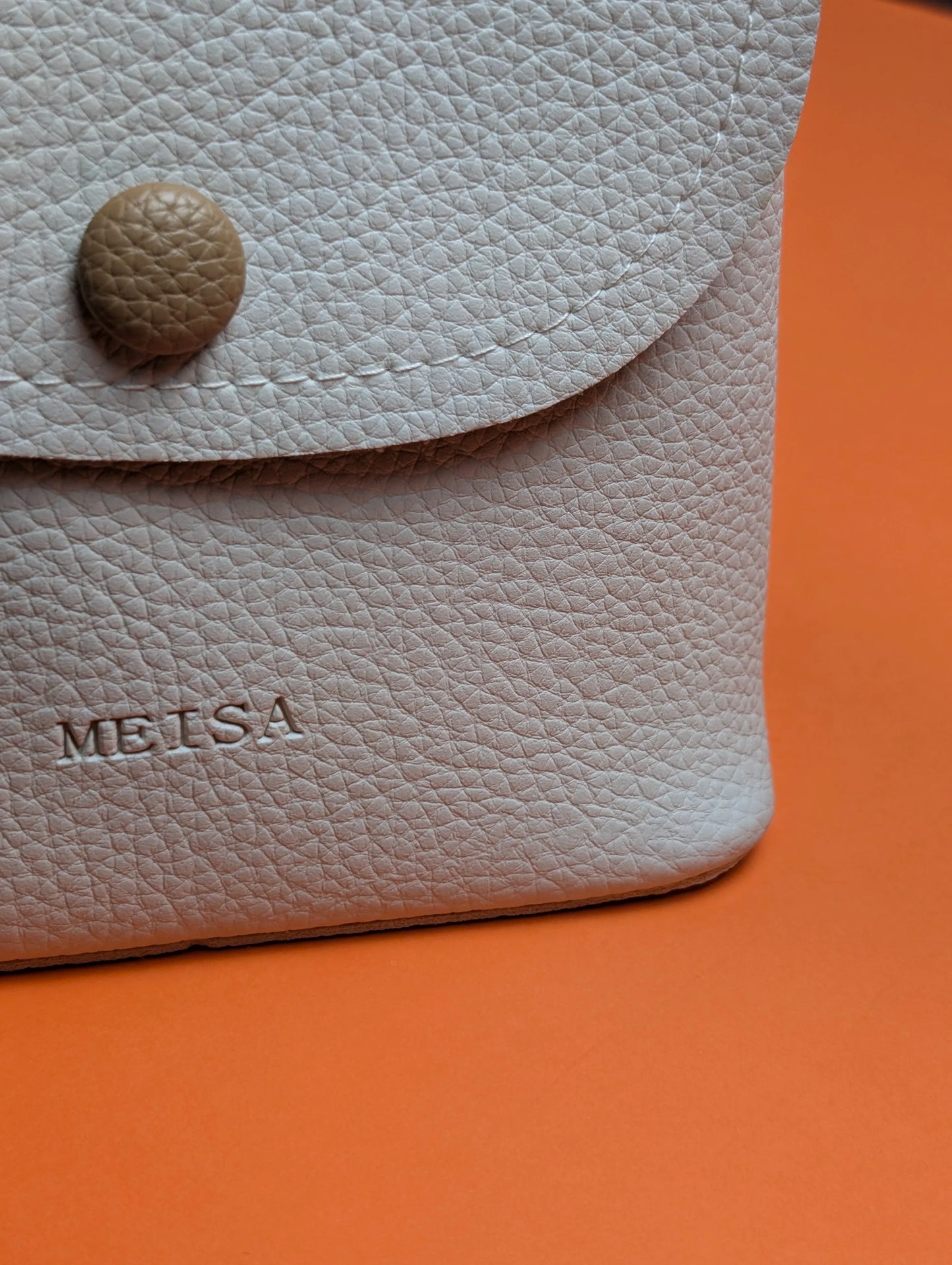 Close-up of beige textured leather wallet with embossed MEISA logo and round button on orange background