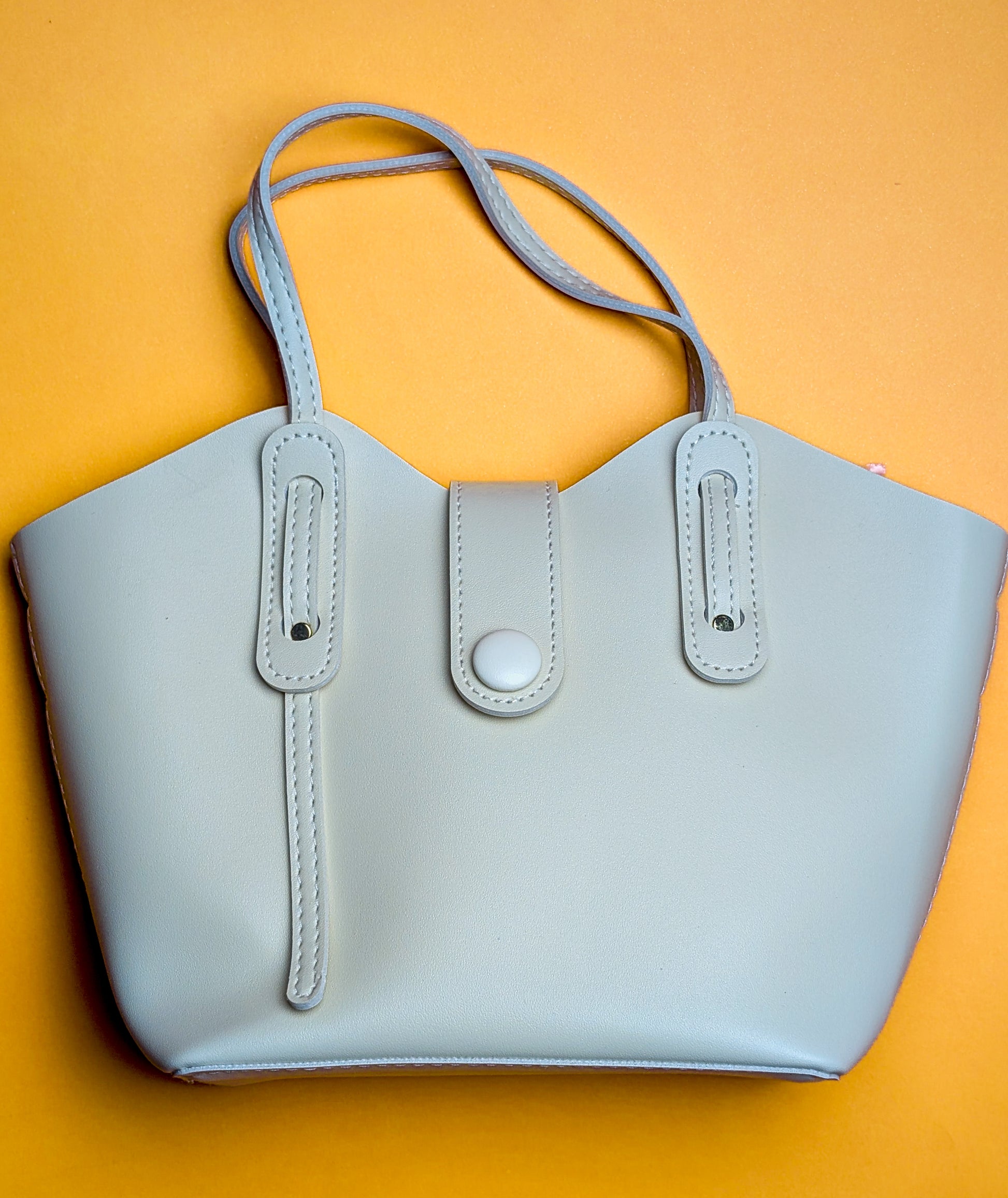 Light gray leather handbag with double straps and button closure on orange background