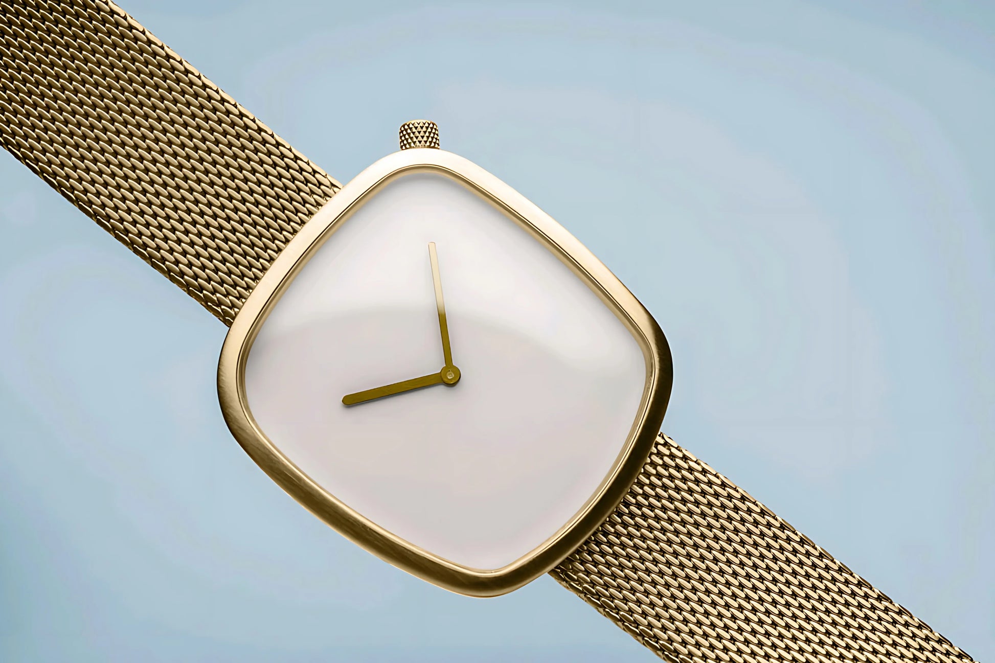 Gold square watch with minimalist white dial and mesh strap on light background