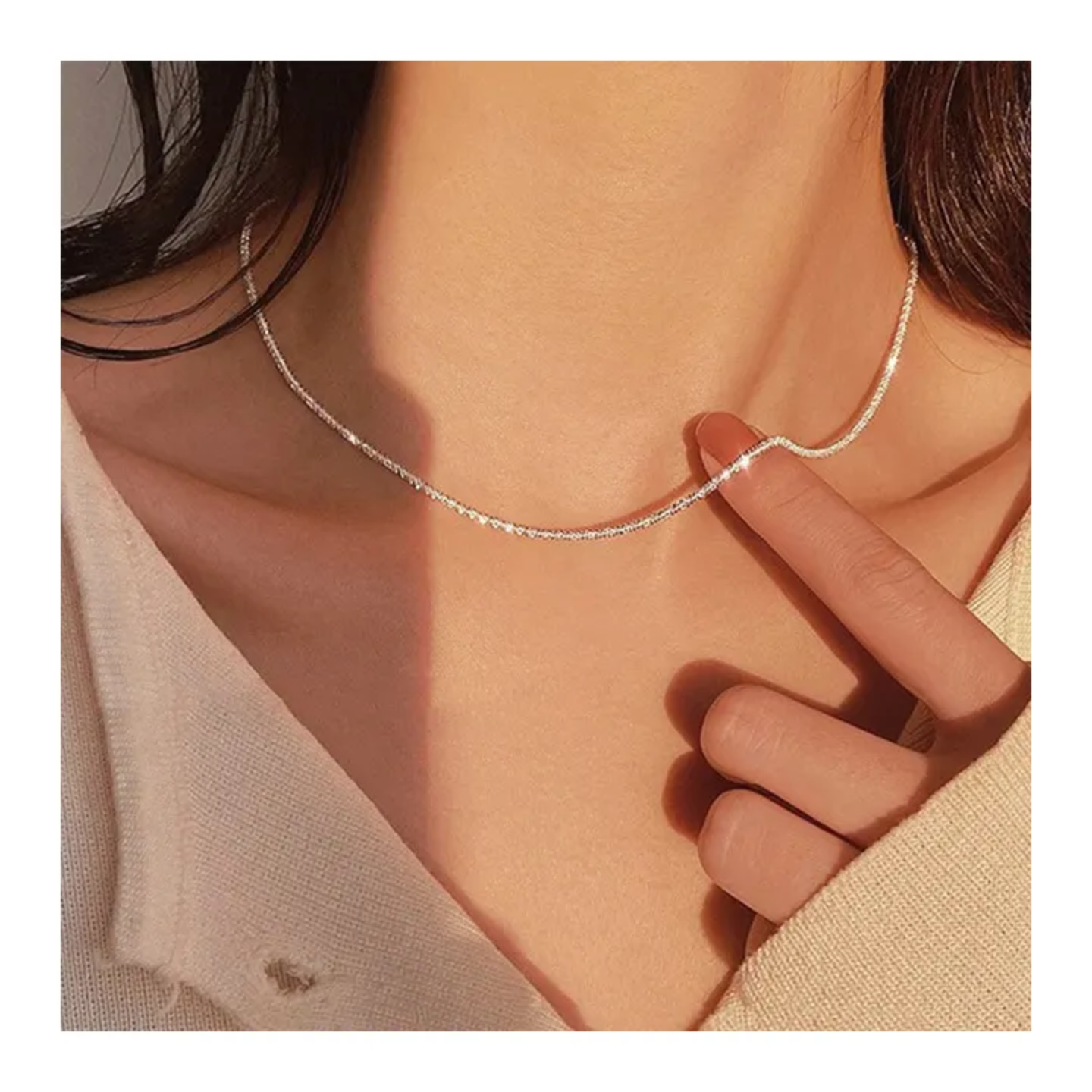 close-up of a woman wearing a delicate silver chain necklace with finger touching it, beige knit sweater