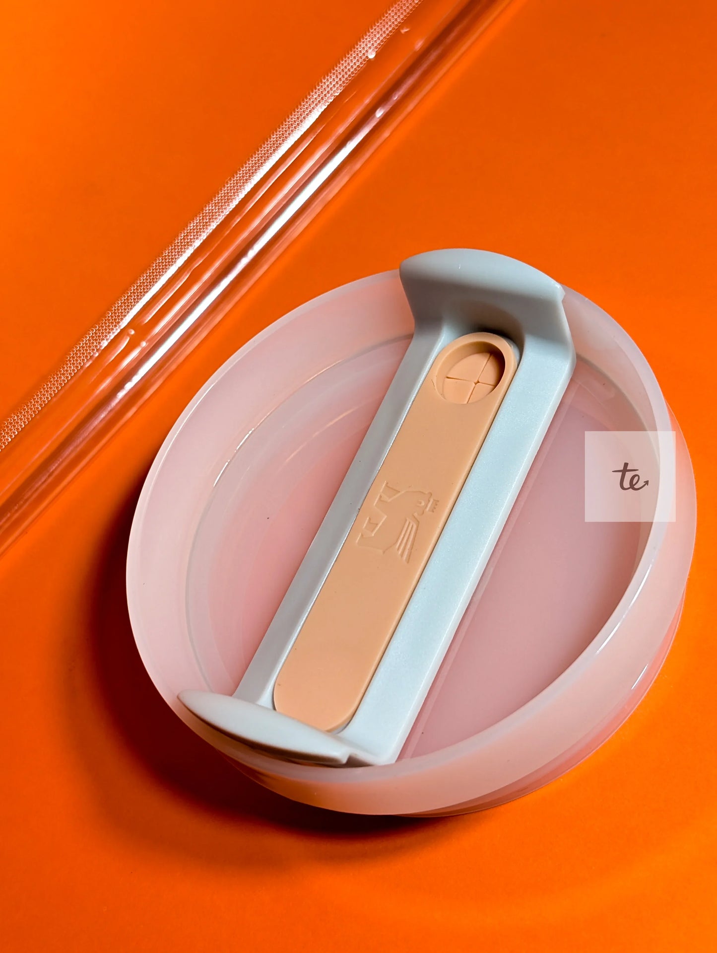 Close-up of a silicone collapsible container lid with a gray and beige locking mechanism on an orange background