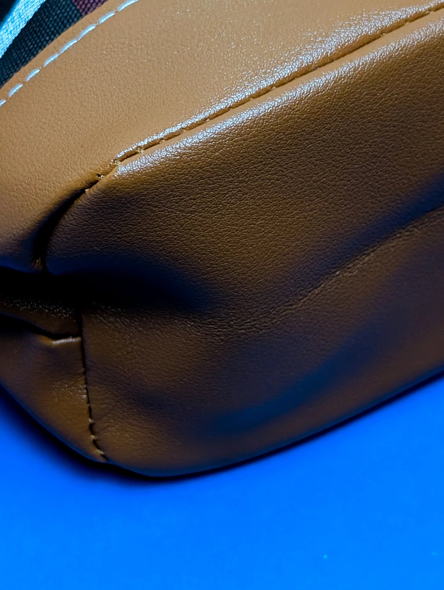 Close-up of brown leather bag corner with detailed stitching on blue surface