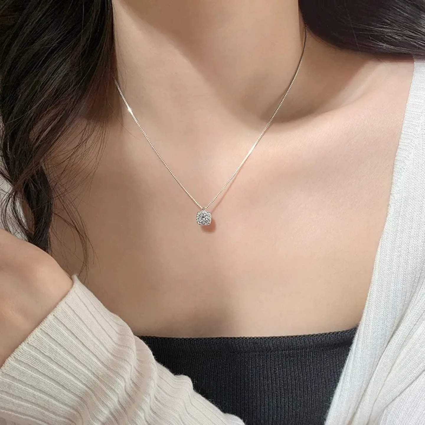 Close-up of a woman wearing a delicate silver necklace with a sparkling diamond pendant