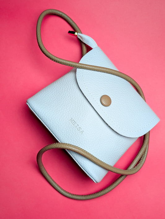 White textured leather crossbody bag with tan strap and button on pink background