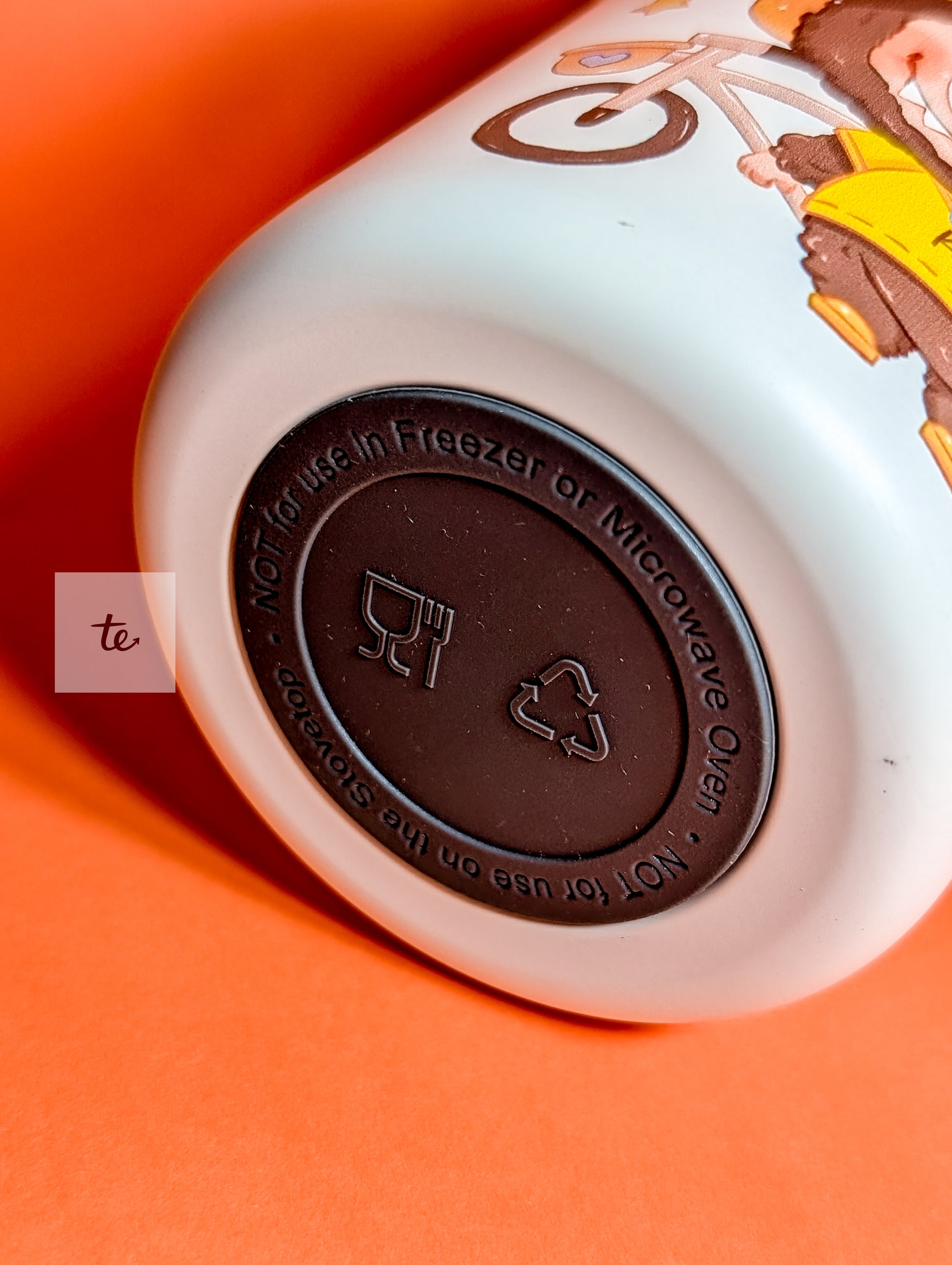 Bottom of a white bottle with black base showing food safe symbol and microwave freezer warning on orange background