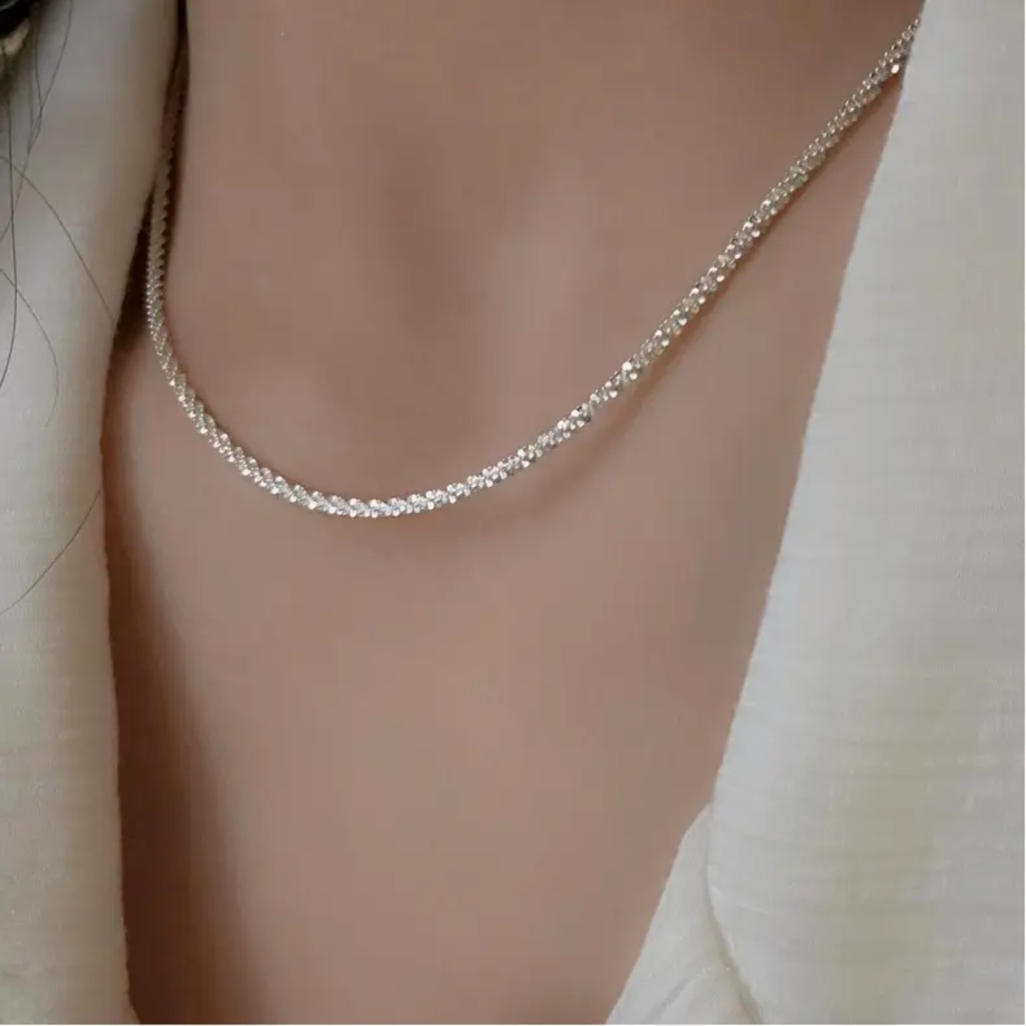 Close-up of a delicate silver chain necklace worn with a white textured top
