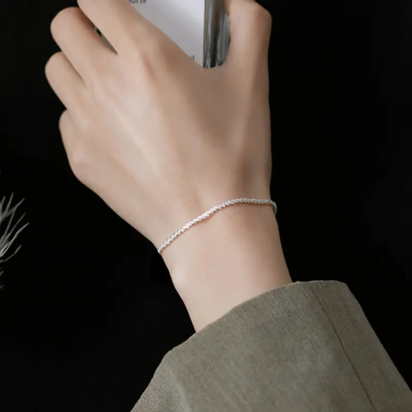 Close-up of a hand wearing a delicate silver bracelet against a black background