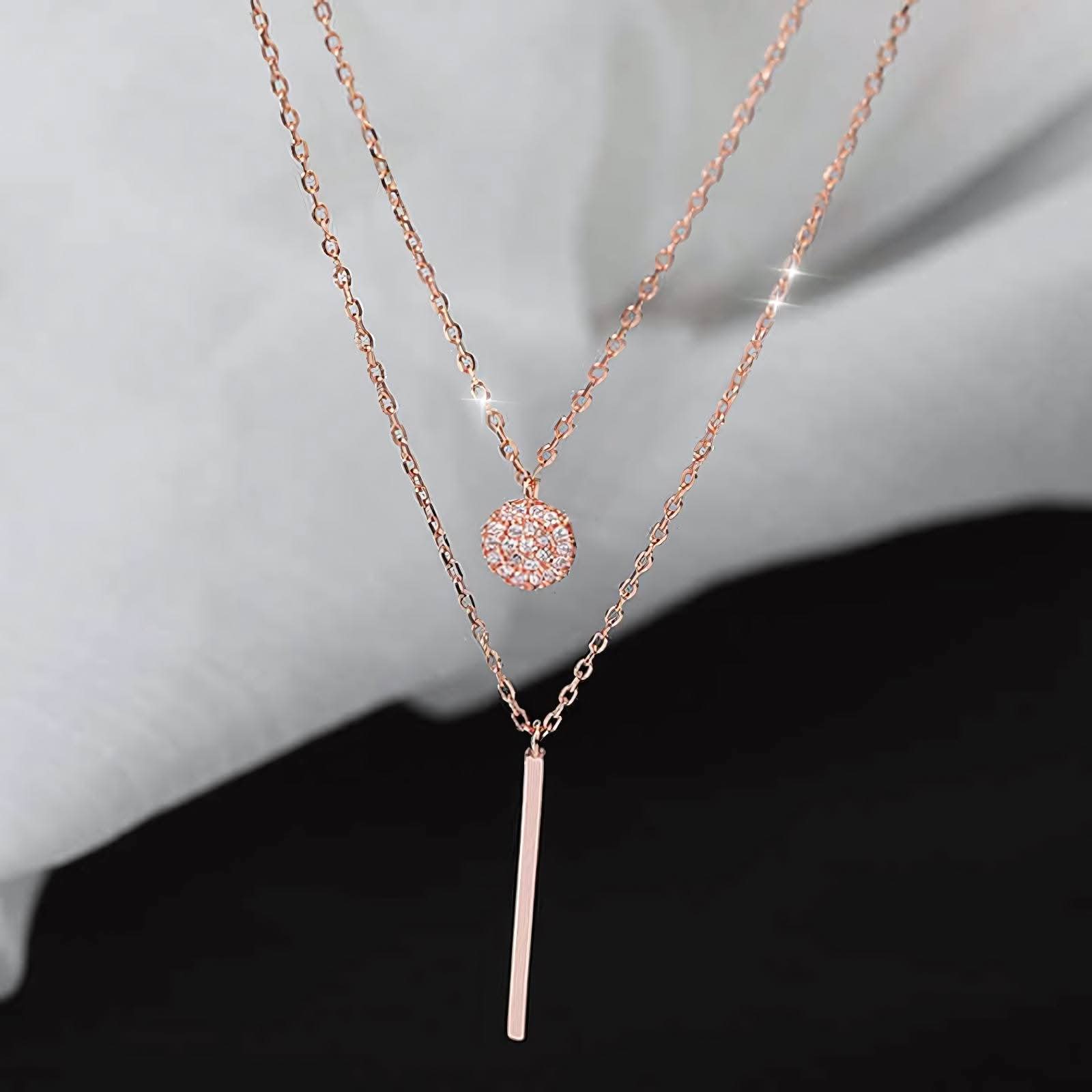 Elegant layered rose gold necklaces with a sparkly round pendant and a sleek bar pendant on a soft gray background