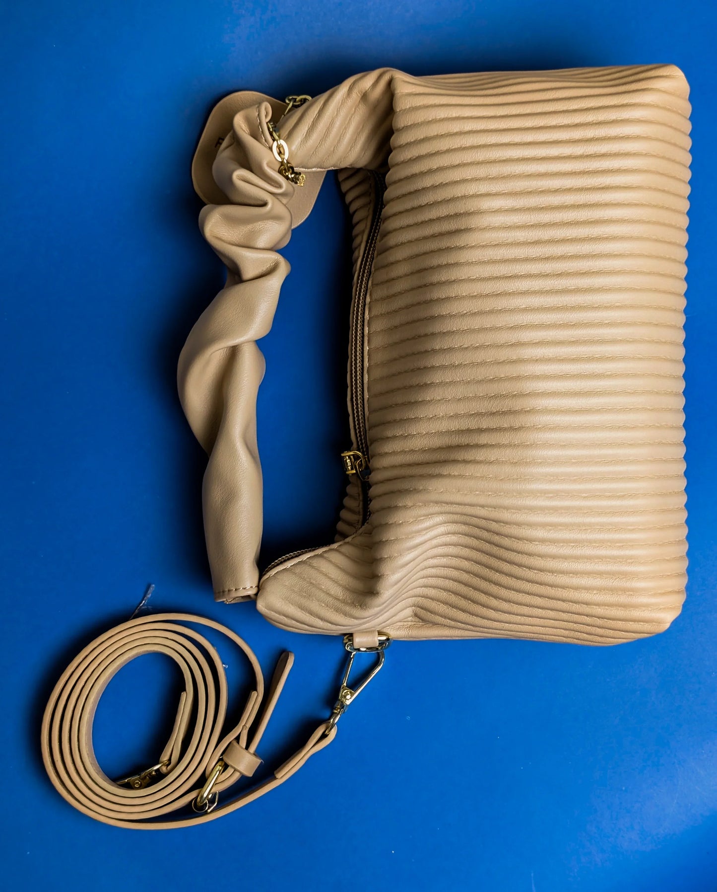 Beige quilted leather handbag with scrunched handle and detachable strap on blue background