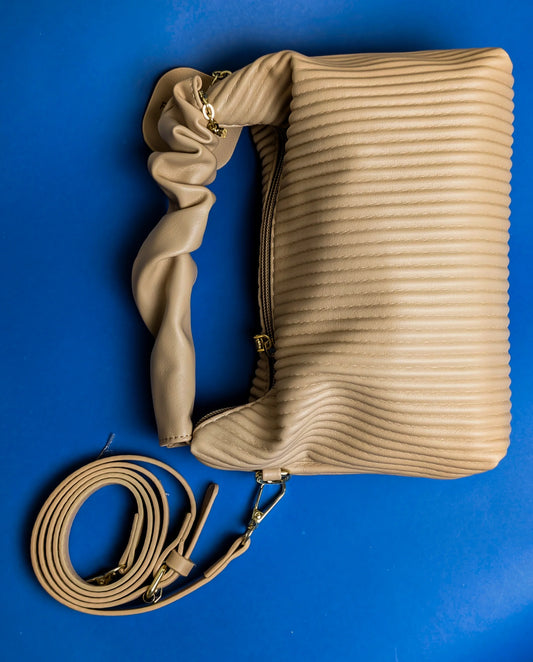 Beige quilted leather handbag with scrunched handle and detachable strap on blue background