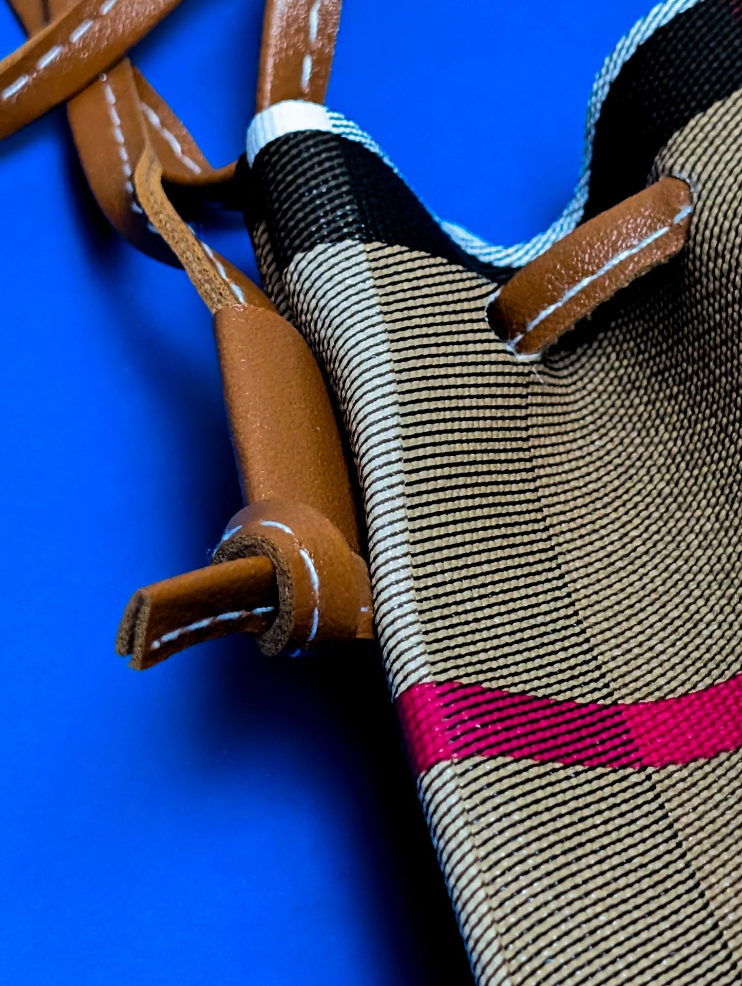 Close-up of brown leather straps and checkered fabric with black, beige, white, and red stripes on blue background