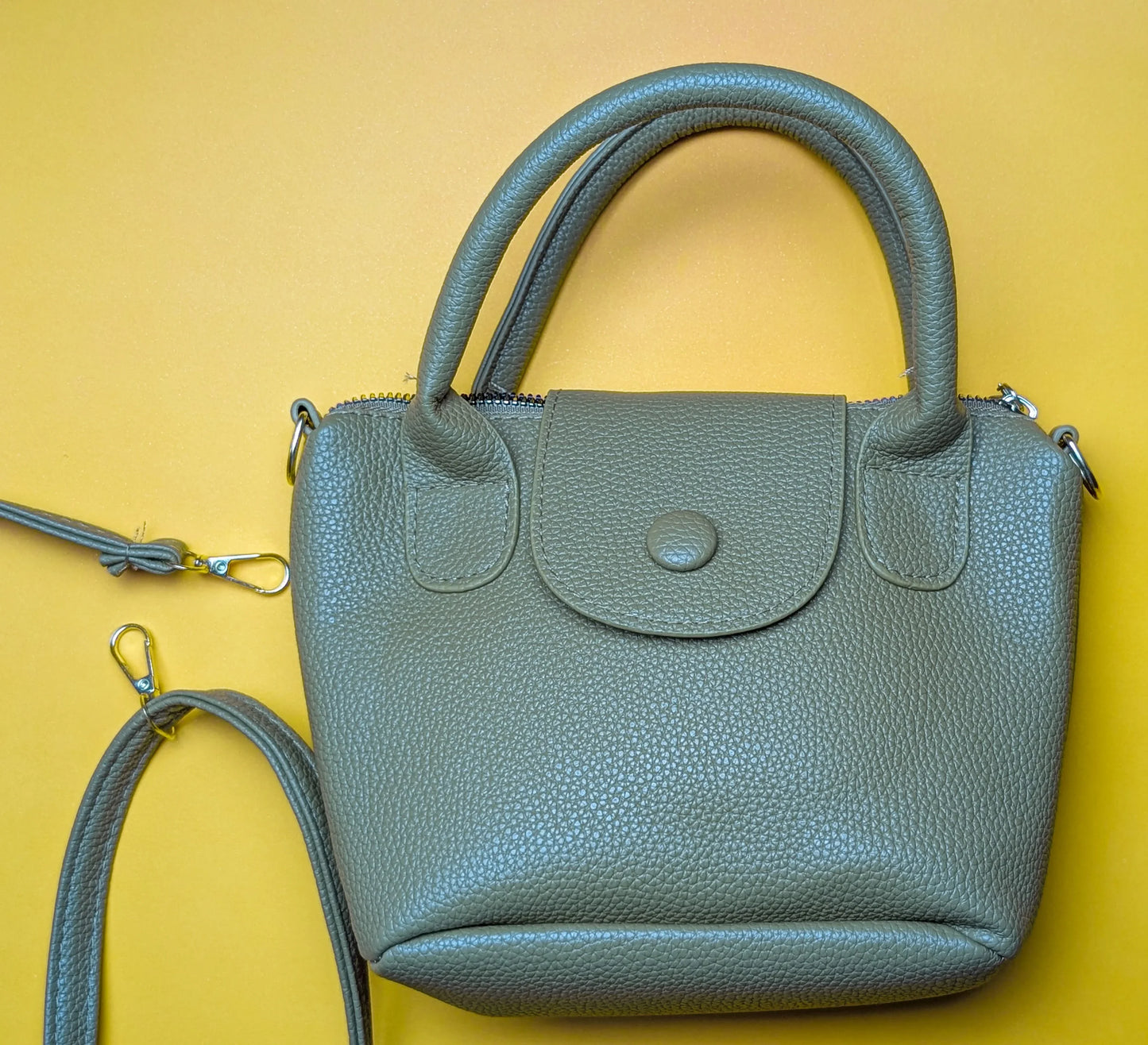 Small gray textured leather handbag with handles and detachable strap on yellow background