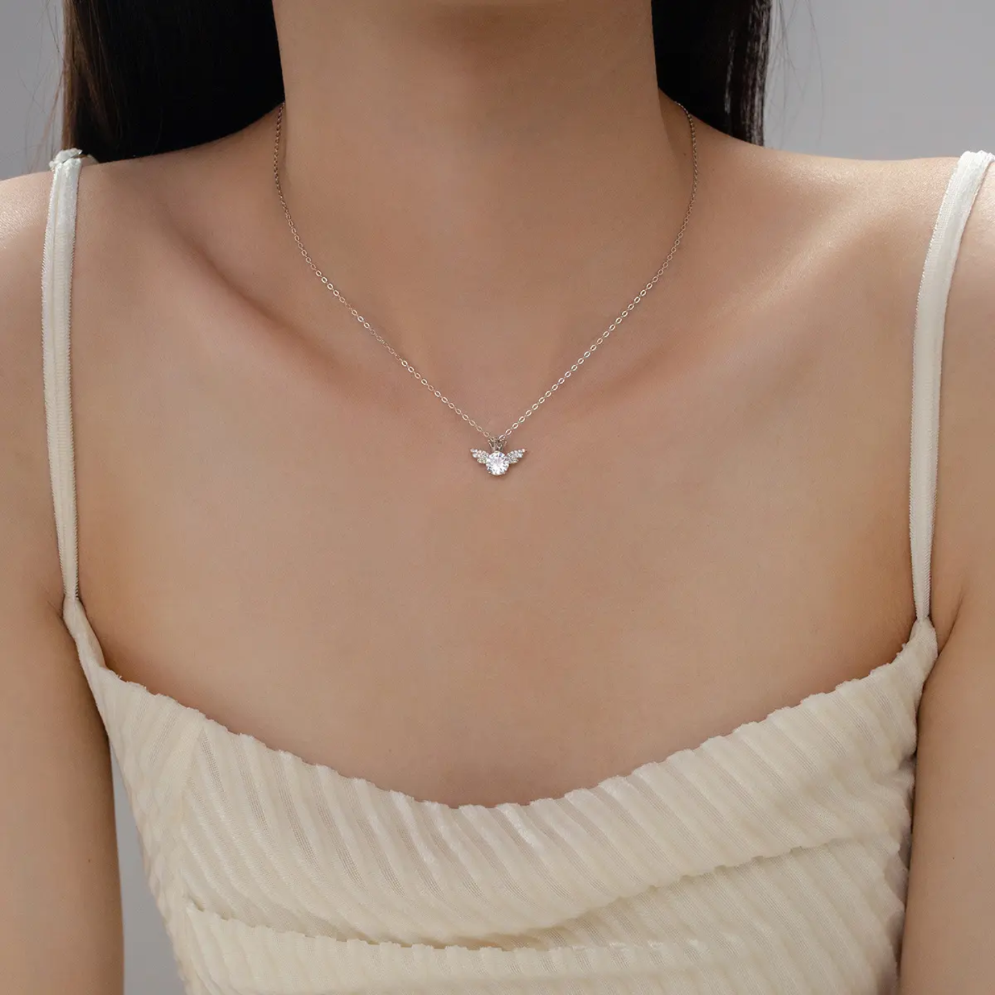 Close-up of woman wearing silver necklace with angel wing pendant and a cream sleeveless top