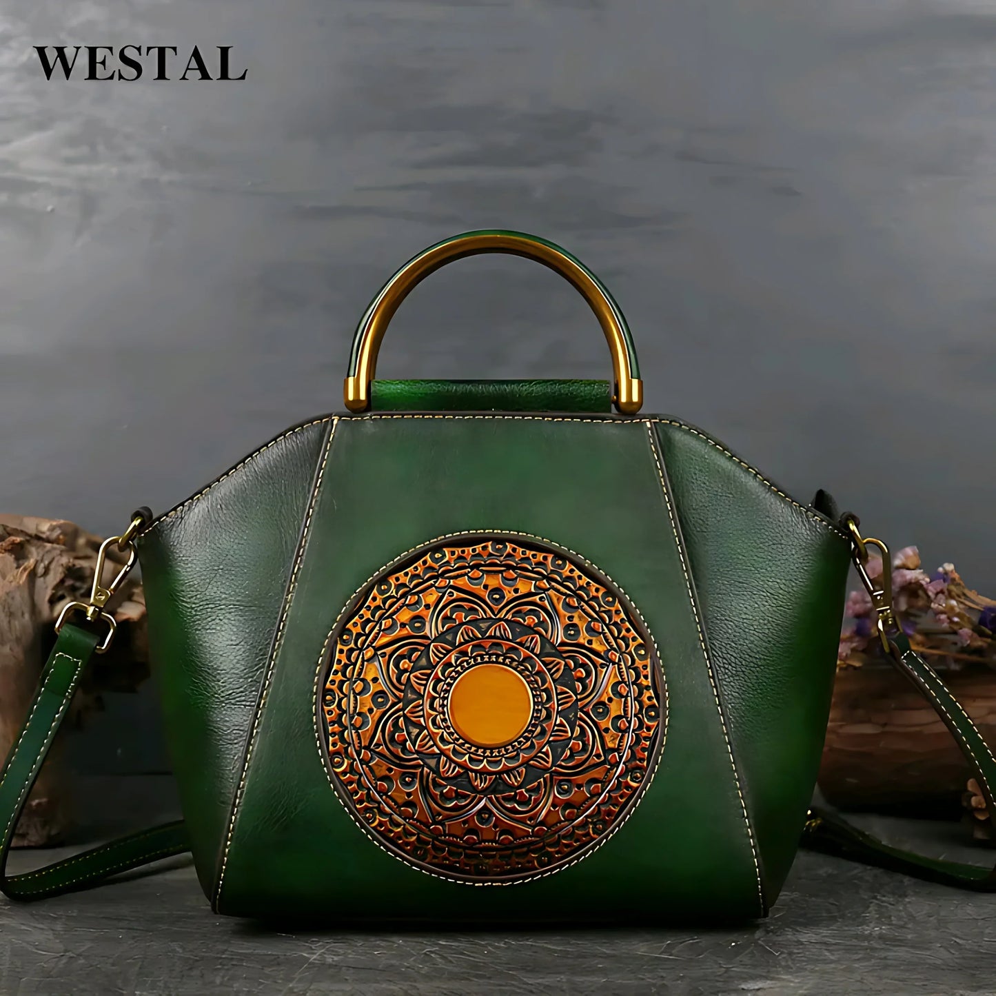 Green leather handbag with gold circular embossed mandala design and metal handle on gray surface