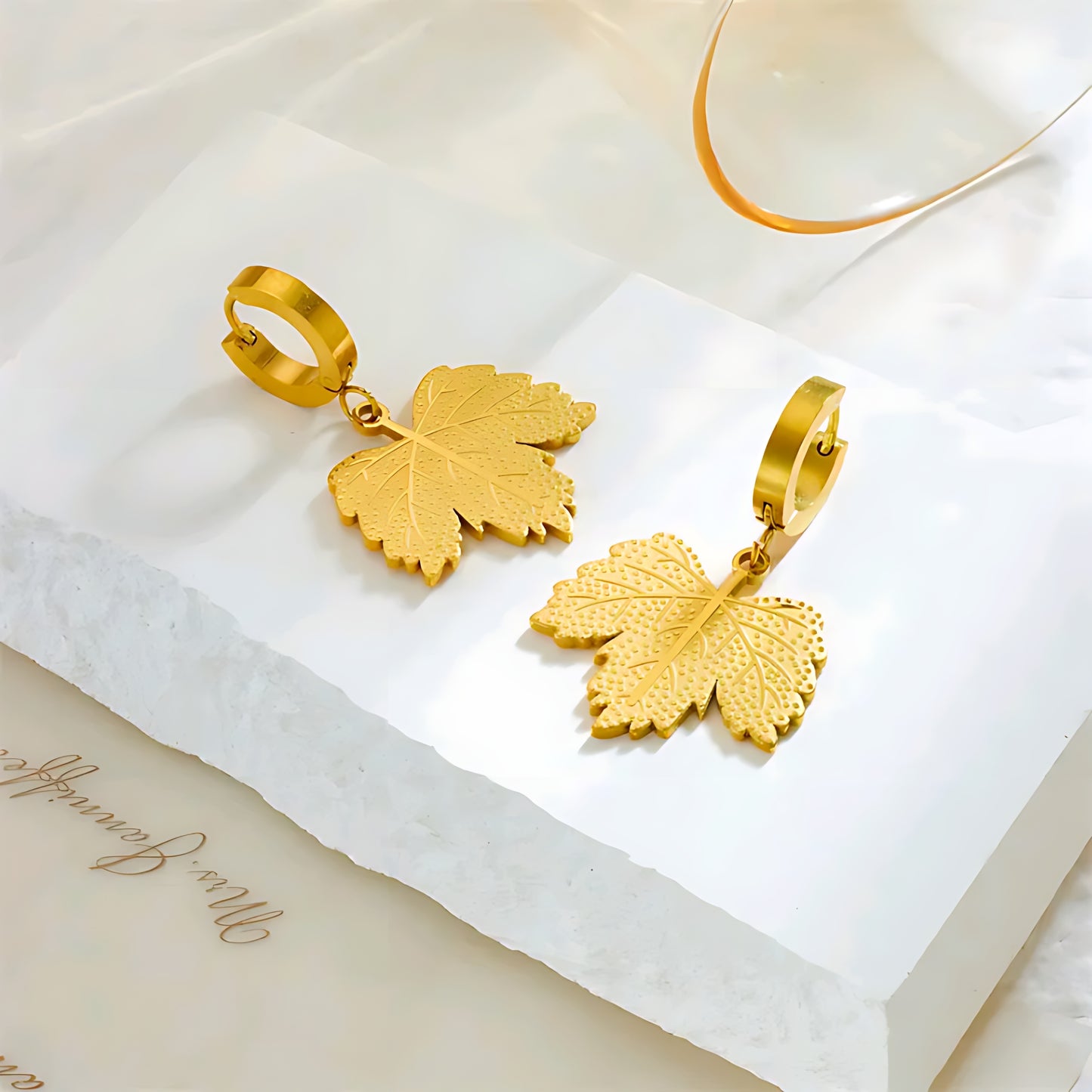 Gold leaf-shaped dangle earrings on white textured surface with soft natural light
