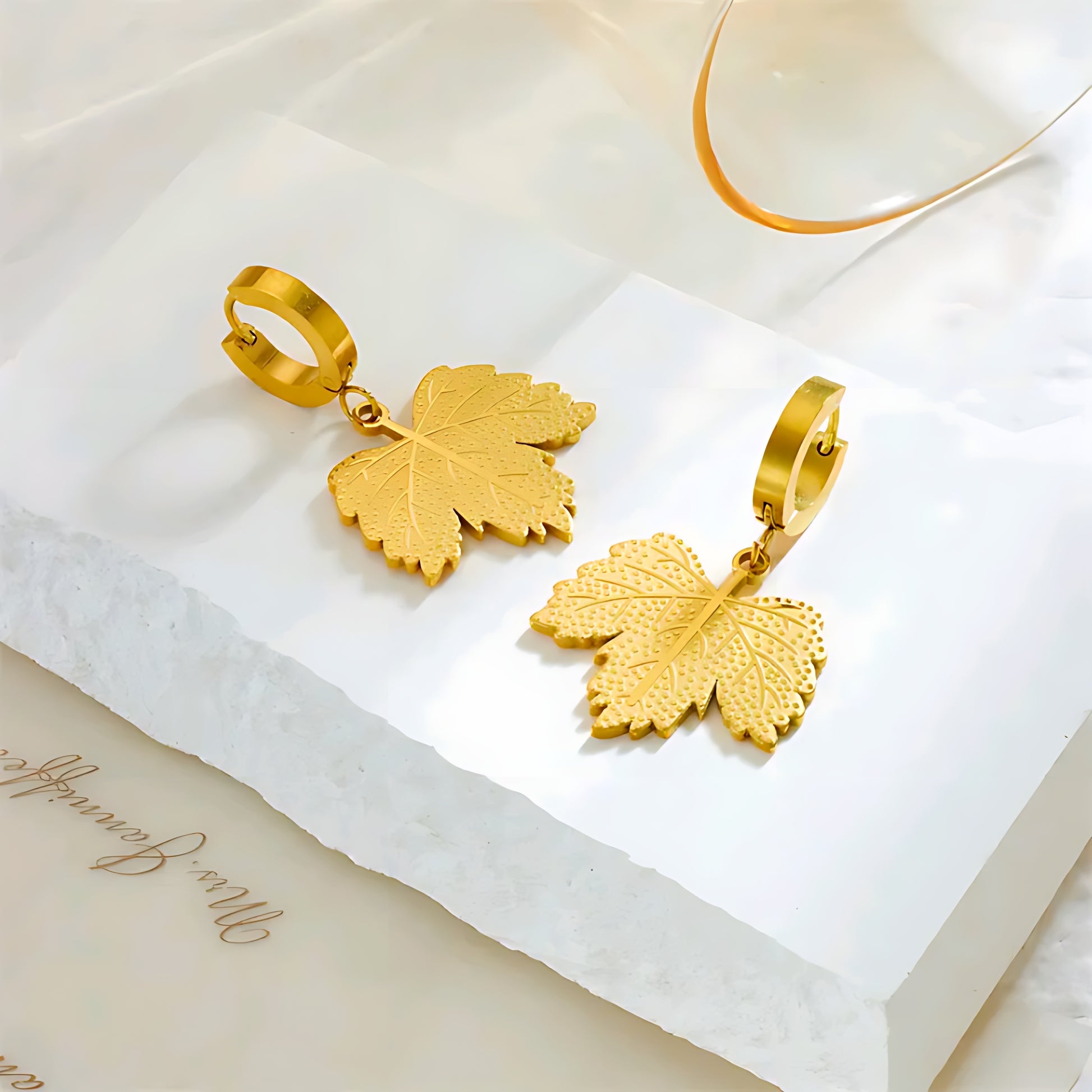 Gold leaf-shaped dangle earrings on white textured surface with soft natural light