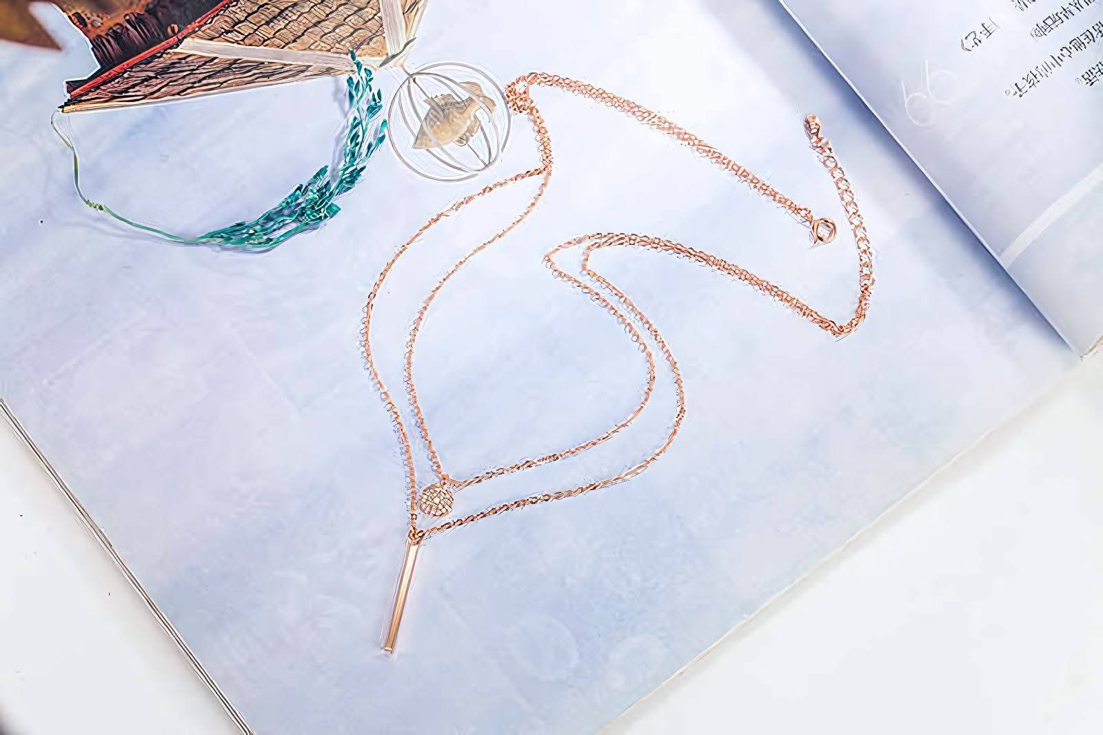 Rose gold layered necklace with geometric pendants on an open magazine page