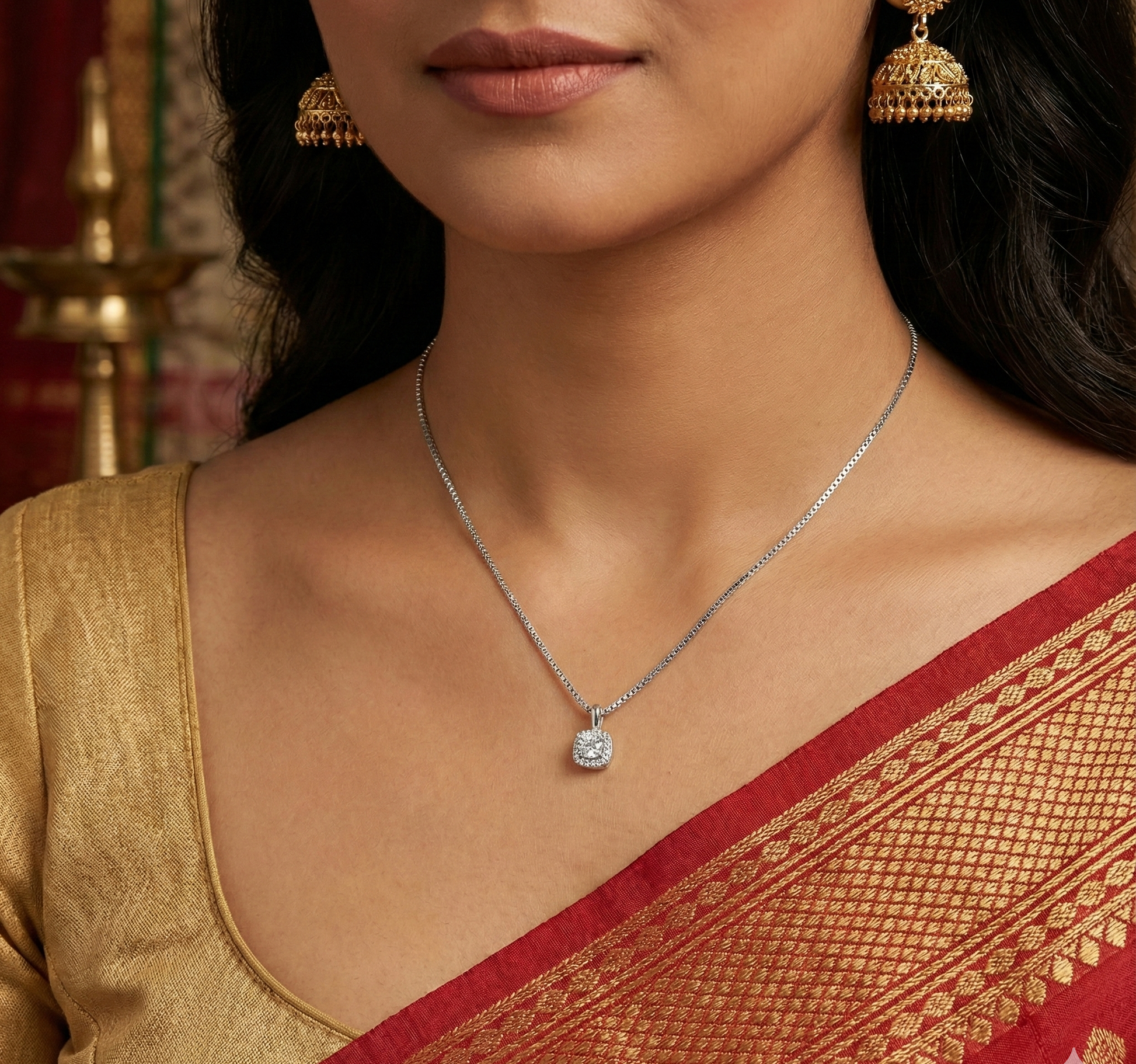 Woman wearing gold jhumka earrings, silver diamond pendant necklace, and red and gold saree blouse