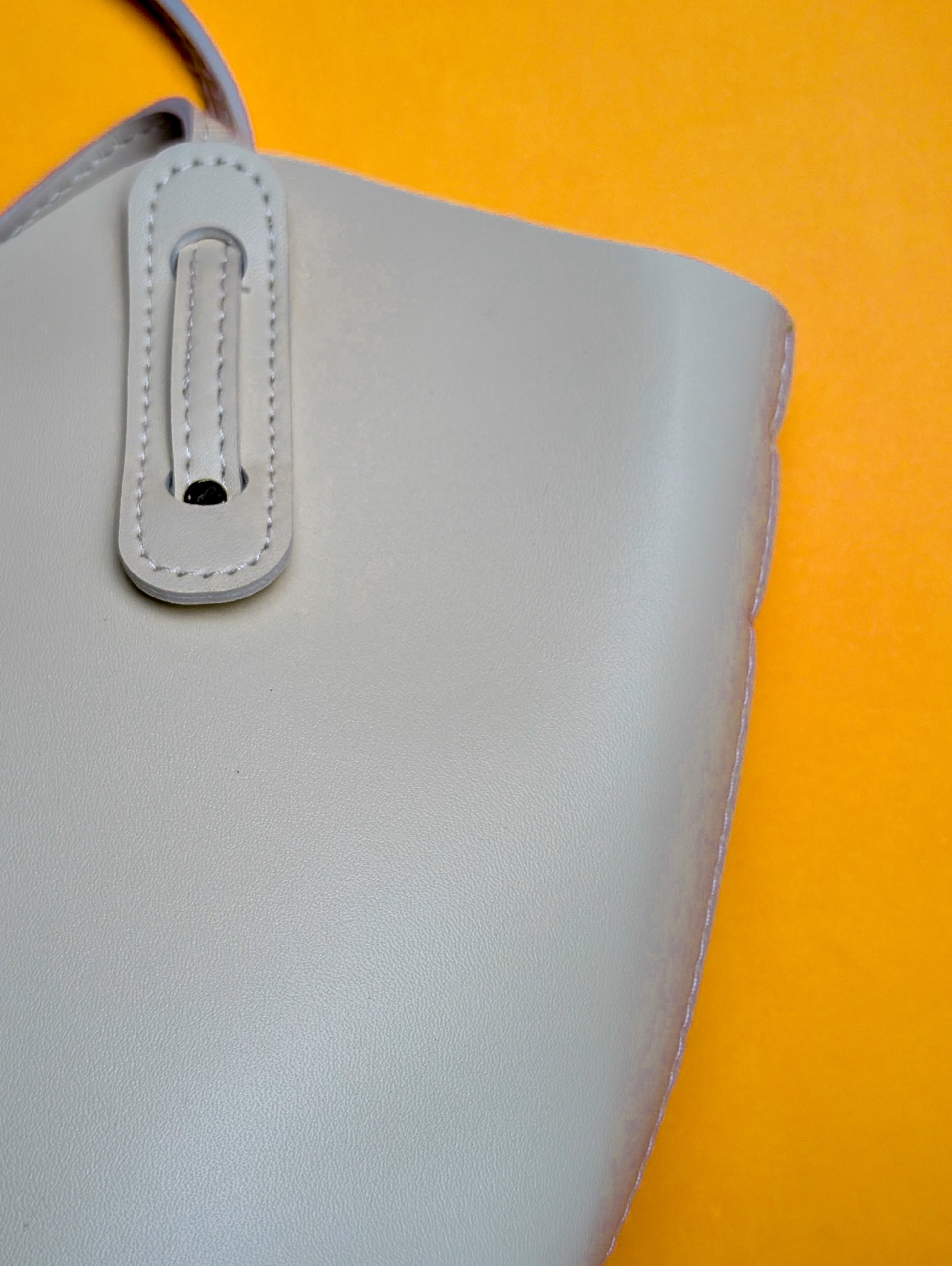 Close-up of a light gray leather handbag strap against a bright orange background