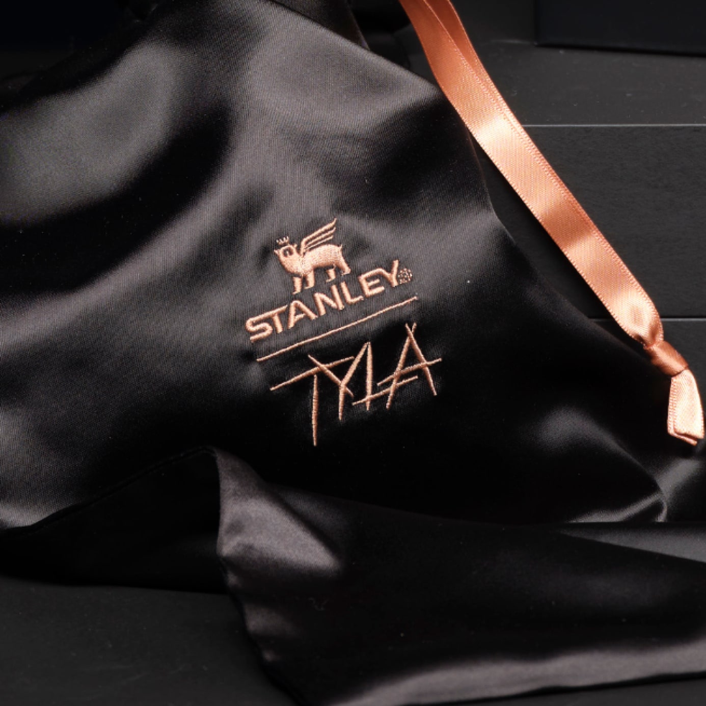 Black satin fabric embroidered with Stanley Tyla logo and copper satin ribbon
